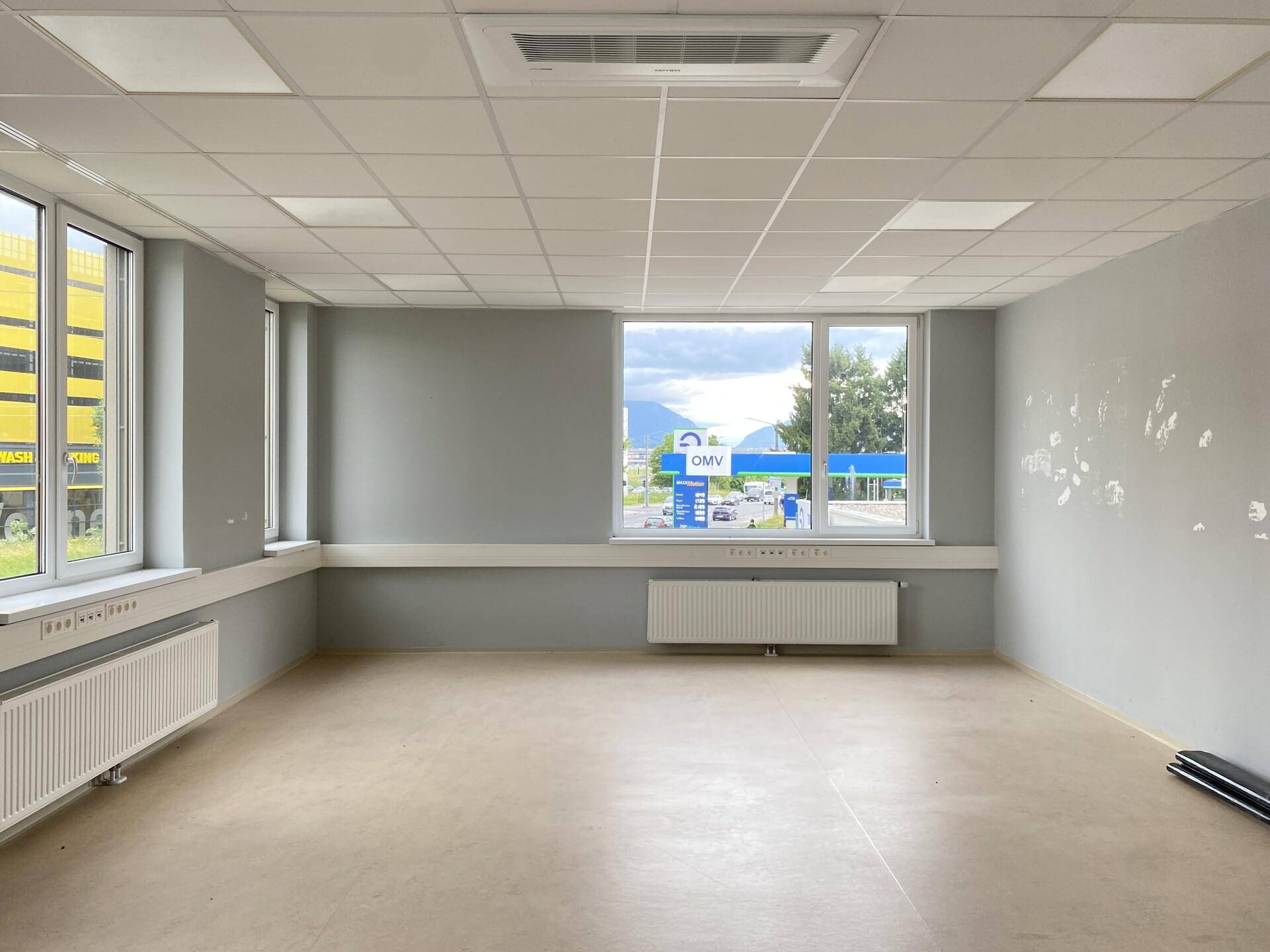 Geräumiger Büroraum mit großen Fenstern, die einen Blick auf die Straße und die Berge im Hintergrund ermöglichen.