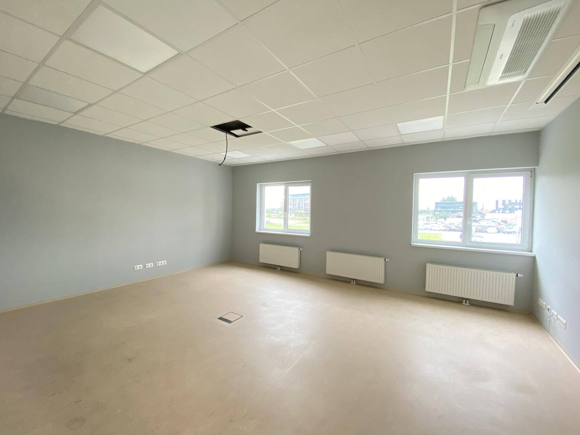 Moderner Büroraum mit abgehängter Decke, integrierter Beleuchtung und Heizkörpern unter den Fenstern.