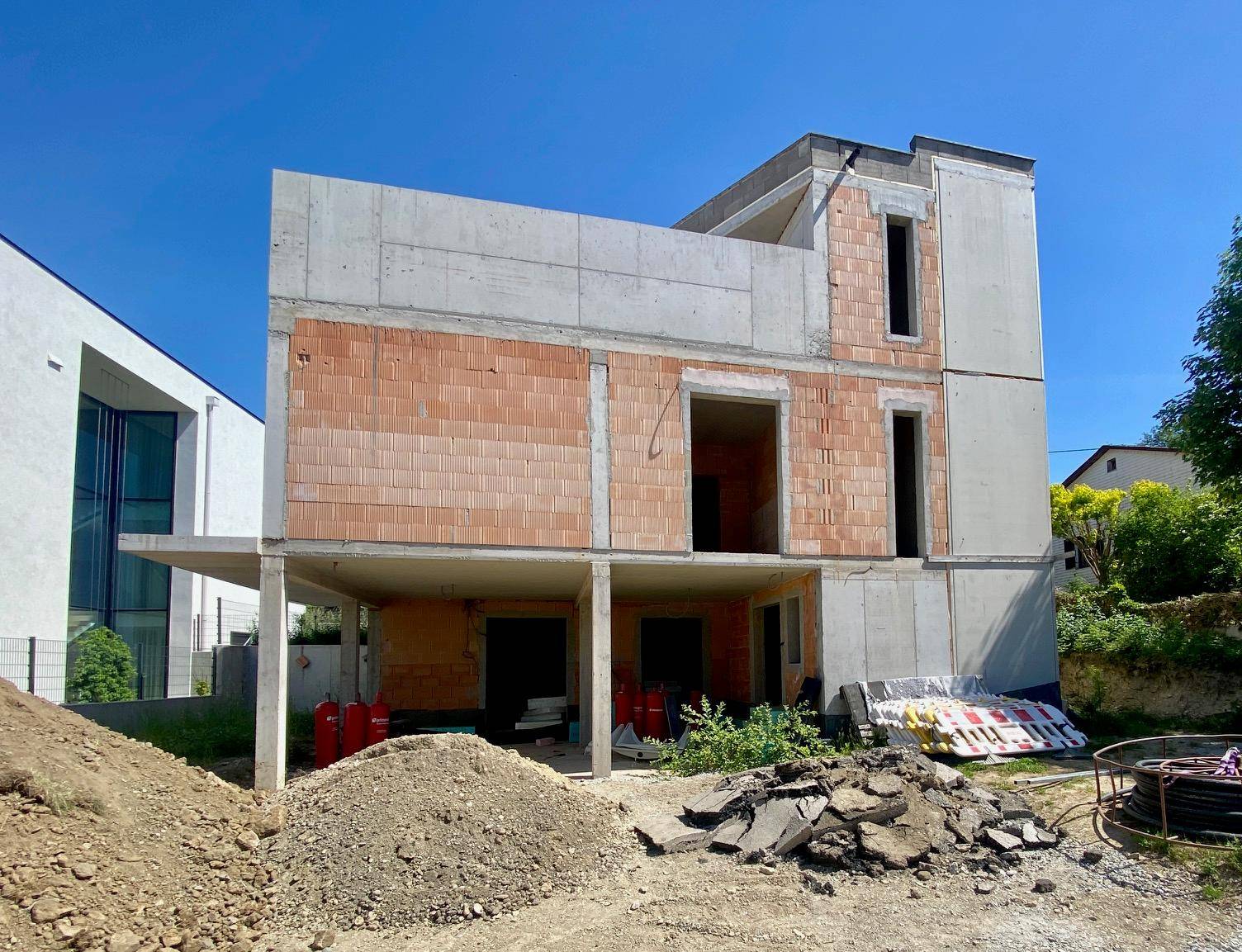 Baustelle eines Hauses im Rohbau mit sichtbaren Beton- und Ziegelstrukturen.
