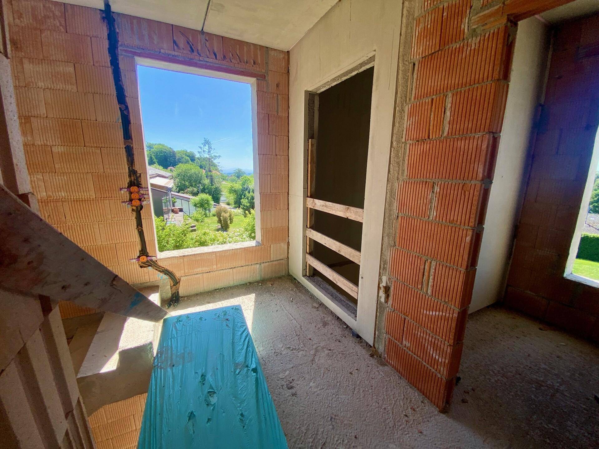 Innenansicht eines Rohbaus mit Ziegelwänden und einem Fenster mit Blick ins Grüne.
