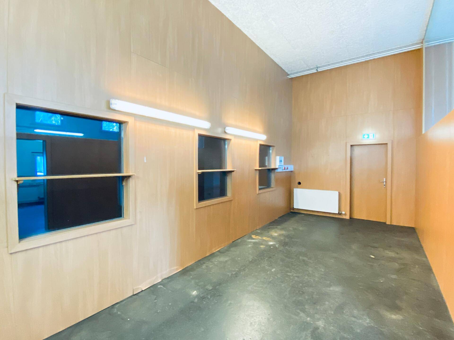 Gewerberaum mit Holzwänden, Betonboden und hohen Fenstern, die Tageslicht hereinlassen.