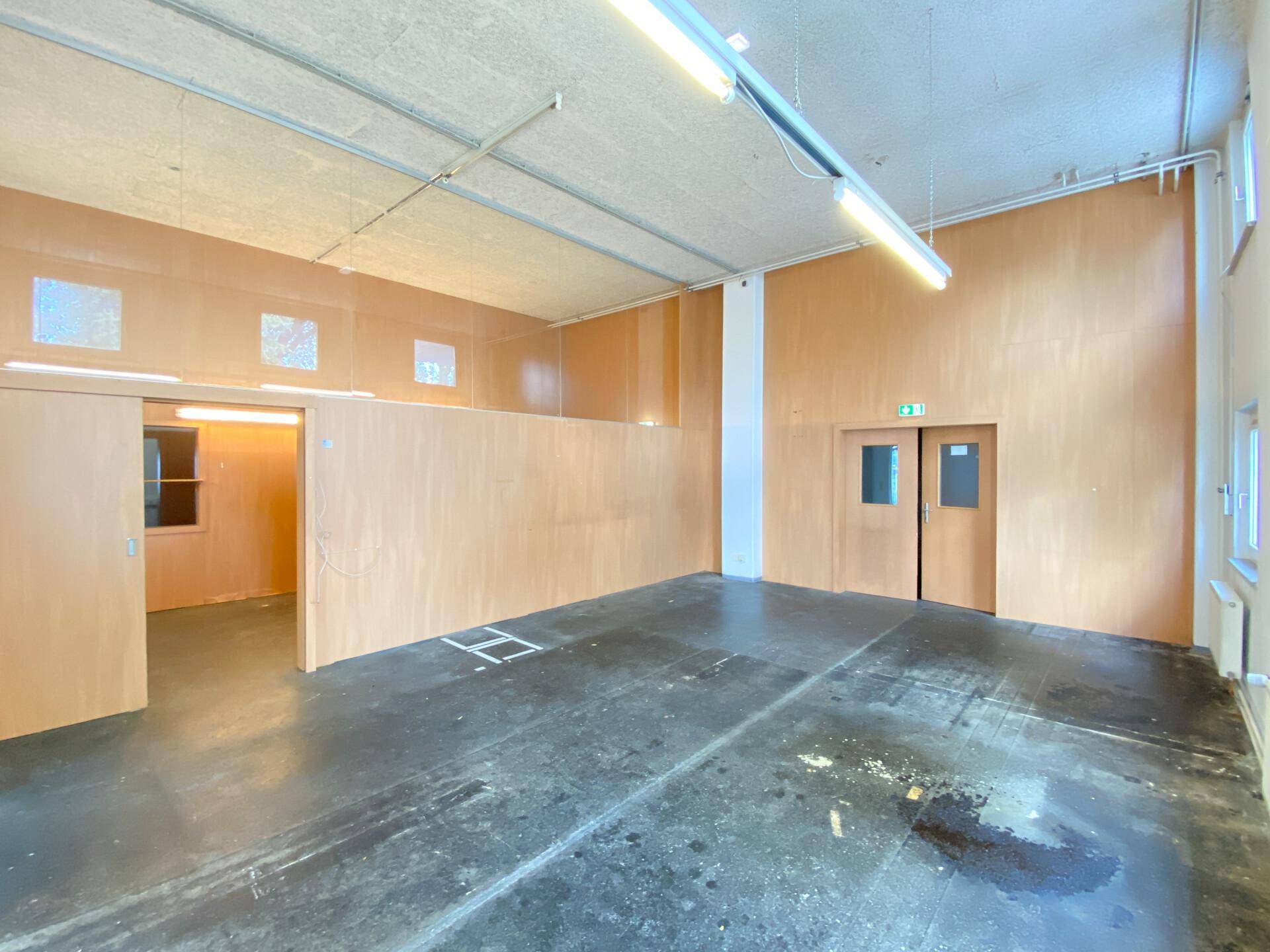 Großer Gewerberaum mit Holzwänden, Betonboden und hohen Decken, bereit zur Nutzung.