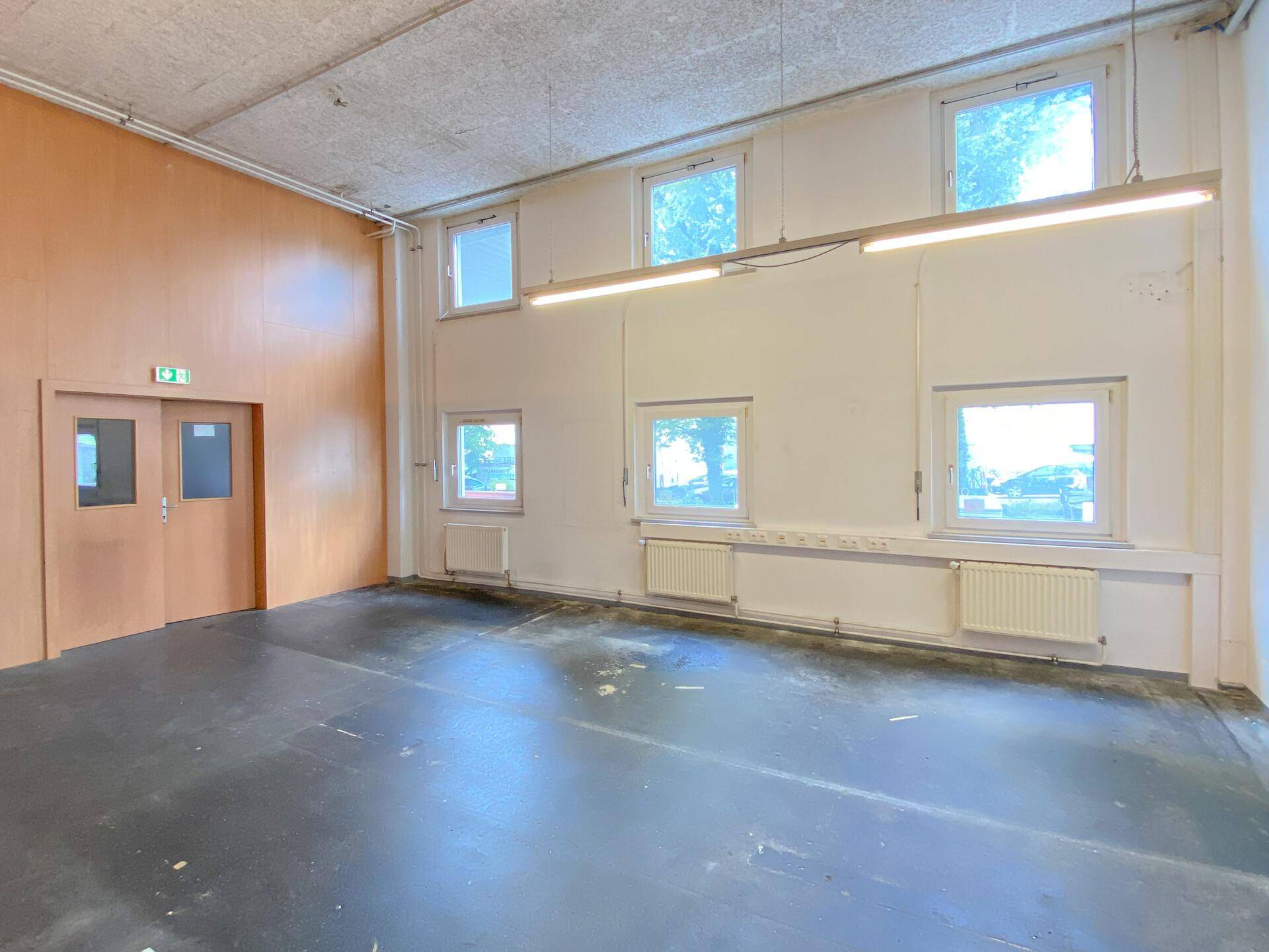 Geräumiger Gewerberaum mit Holzwänden, Betonboden und einer Reihe von Fenstern.