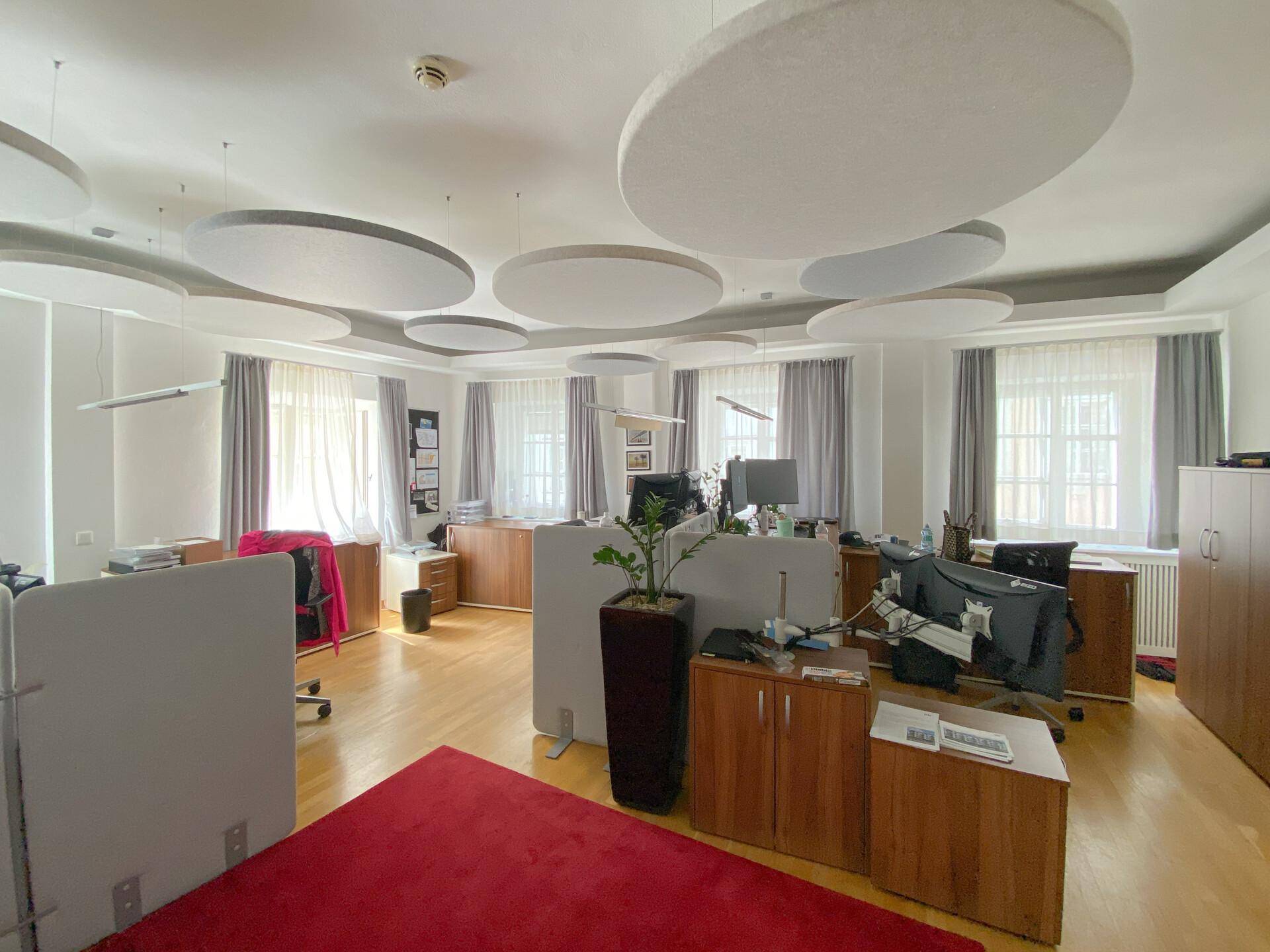 Geräumiges Büro mit Holzfußboden, modernen Schreibtischen und schallabsorbierenden Elementen an der Decke.