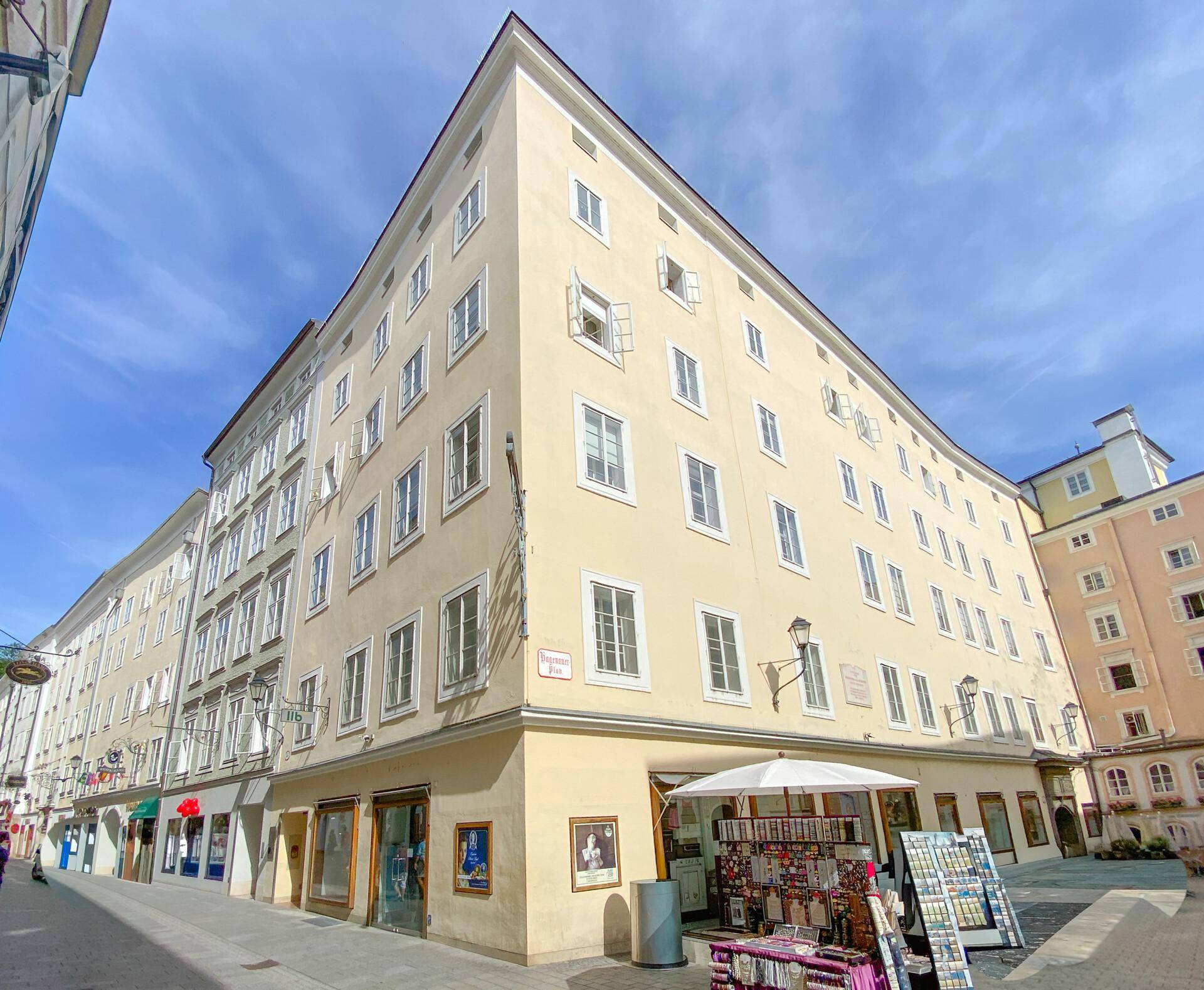Historisches Gebäude mit gelber Fassade, vielen Fenstern und Geschäften im Erdgeschoss in einer Stadtansicht.