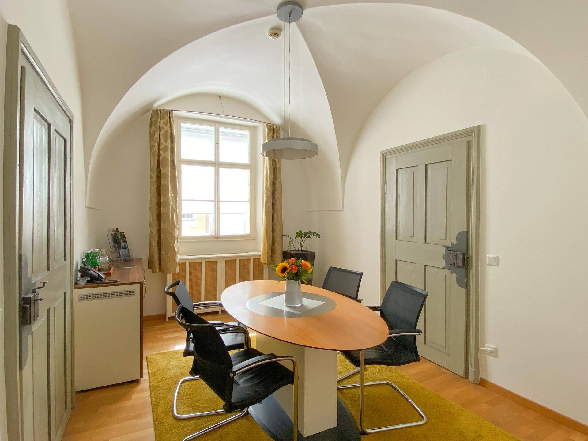 Kleiner Besprechungsraum mit Gewölbedecke, Holzboden und einem Fenster mit Blick nach draußen.