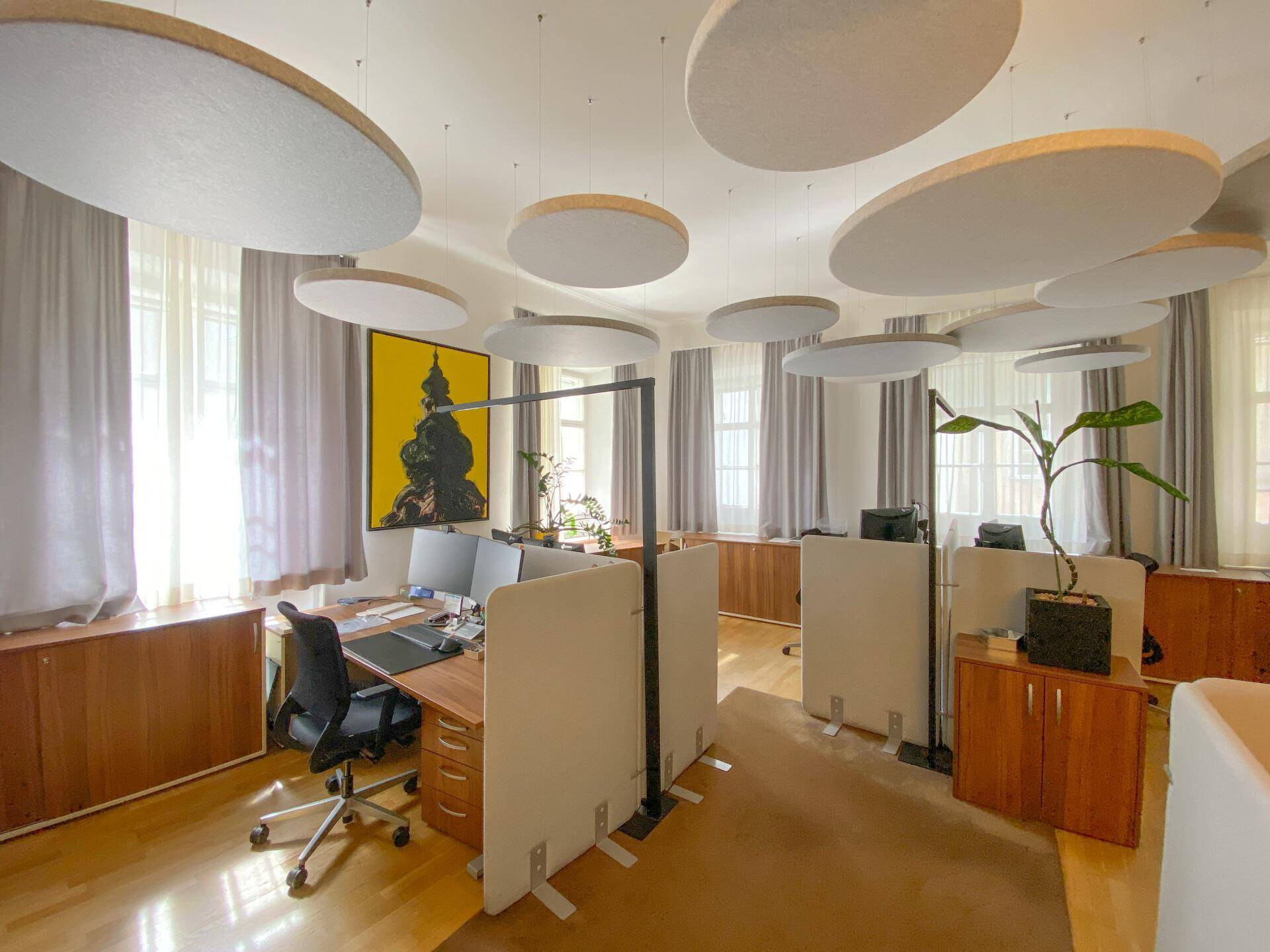 Helles Großraumbüro mit modernen Arbeitsplätzen, schallabsorbierenden Elementen an der Decke und viel Tageslicht.