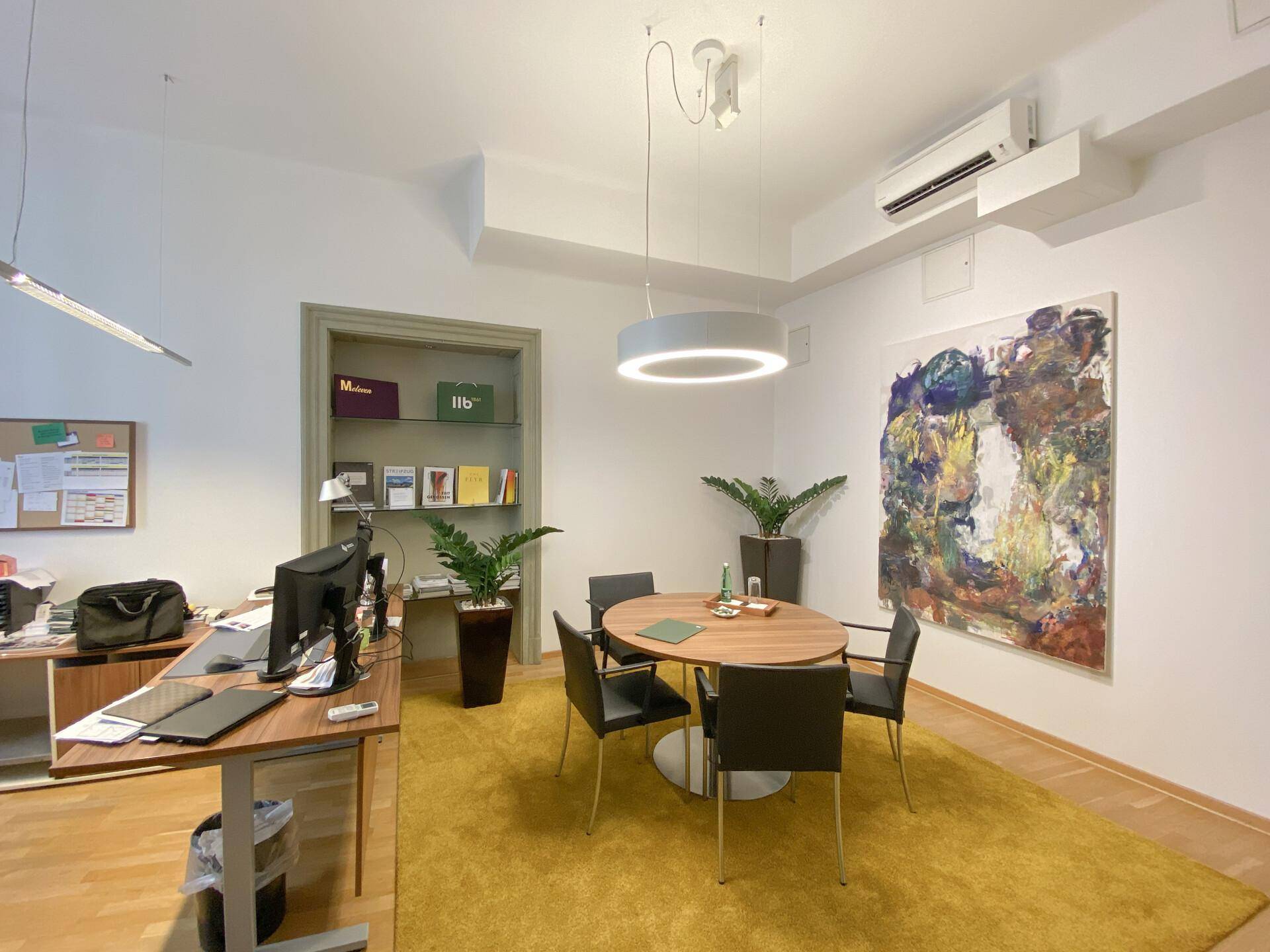 Modernes Büro mit rundem Besprechungstisch, Klimaanlage und einem farbenfrohen Kunstwerk an der Wand.