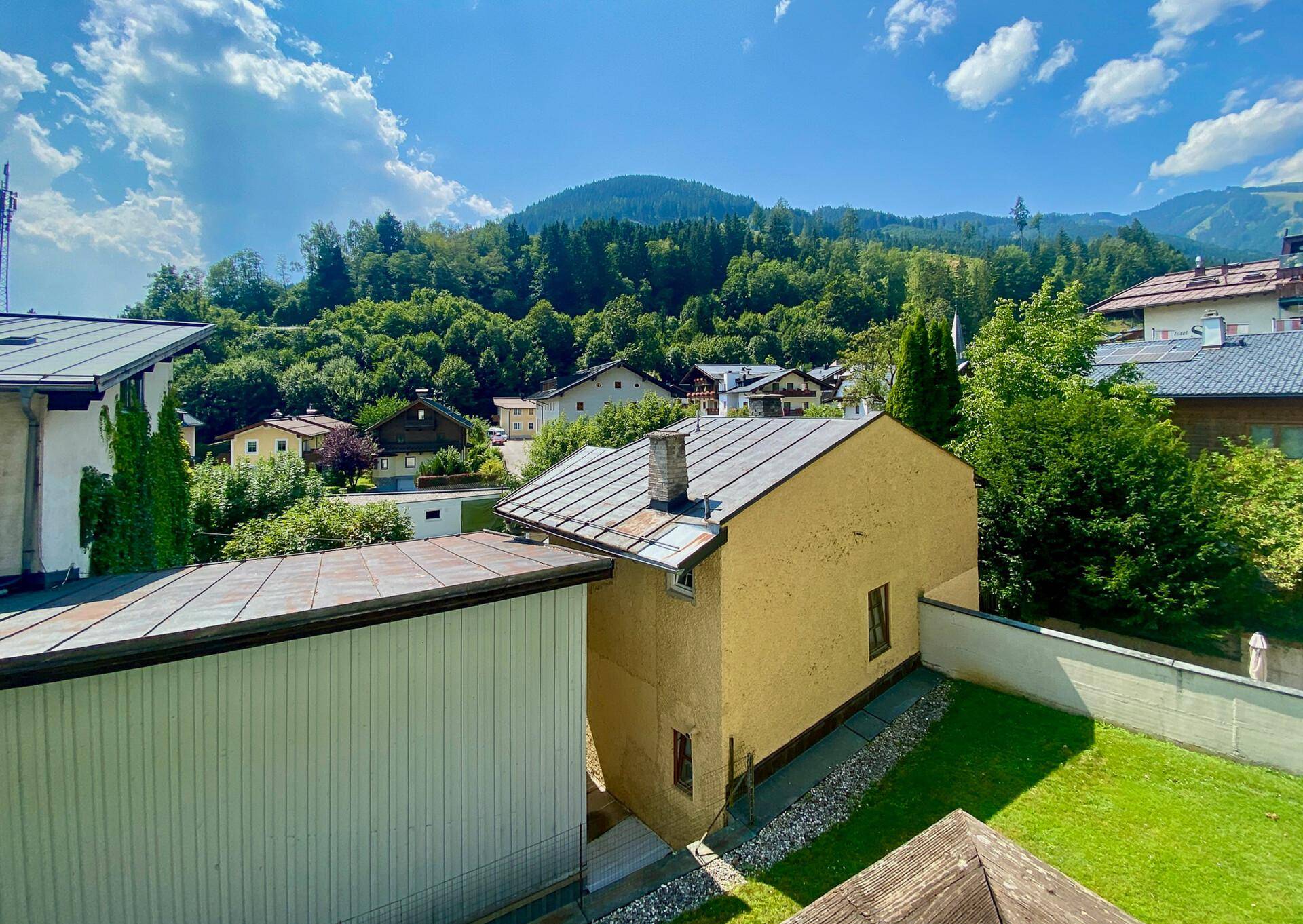 Panoramablick auf die umliegende Berglandschaft und benachbarte Häuser mit grünen Gärten.