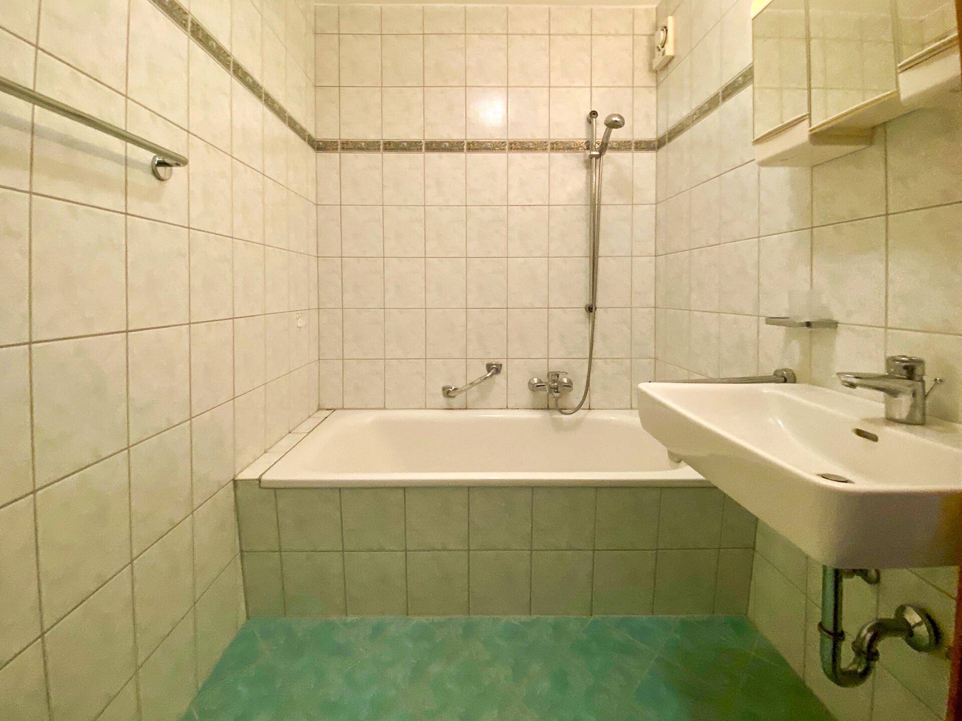 Gefliestes Badezimmer mit Badewanne, Duschvorrichtung und Waschbecken, in einem älteren Stil.