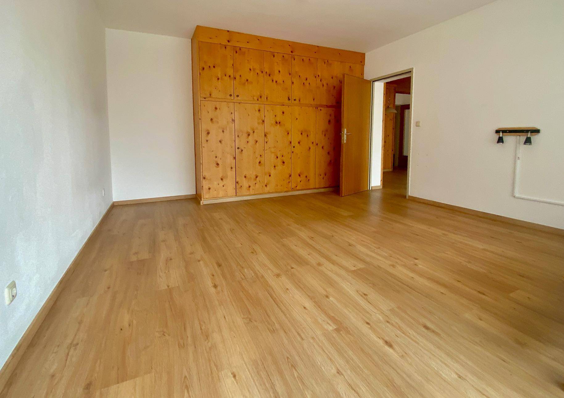 Schlafzimmer mit Holzboden und einer großen, holzvertäfelten Einbauschrankwand, die viel Stauraum bietet.