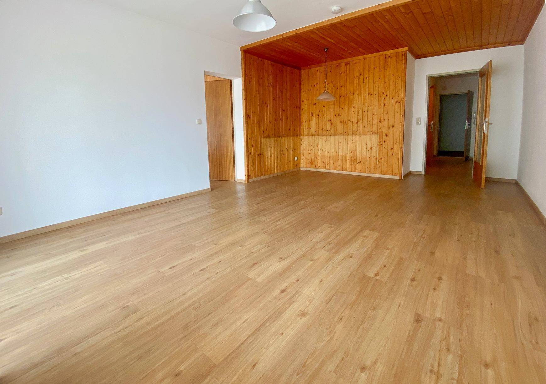 Wohnbereich mit Holzboden, weißen Wänden und einer Holzwandverkleidung, die einen gemütlichen Akzent setzt.