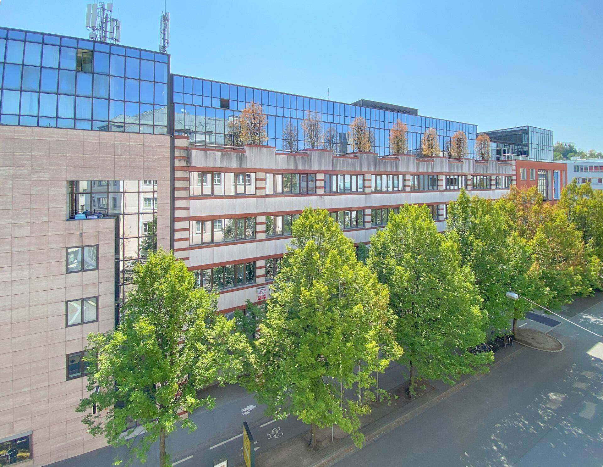 Modernes Bürogebäude mit Glasfassade, mehreren Etagen und Bäumen entlang der Straße.