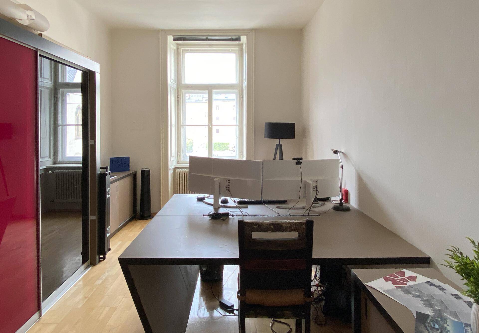 Weiteres Büro mit großem Schreibtisch, mehreren Monitoren und einem auffälligen roten Schiebetürenschrank.
