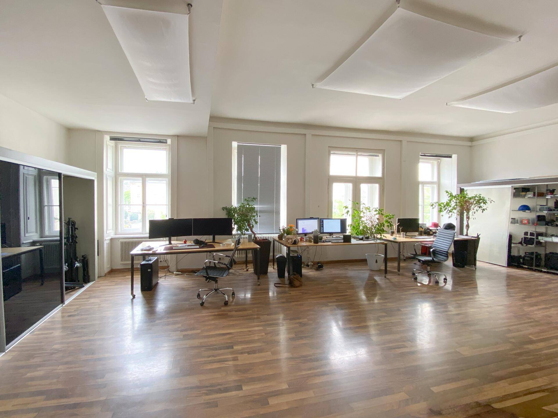 Heller und geräumiger Bürobereich mit Holzboden, modernen Arbeitsplätzen und großen Fenstern für optimale Beleuchtung.