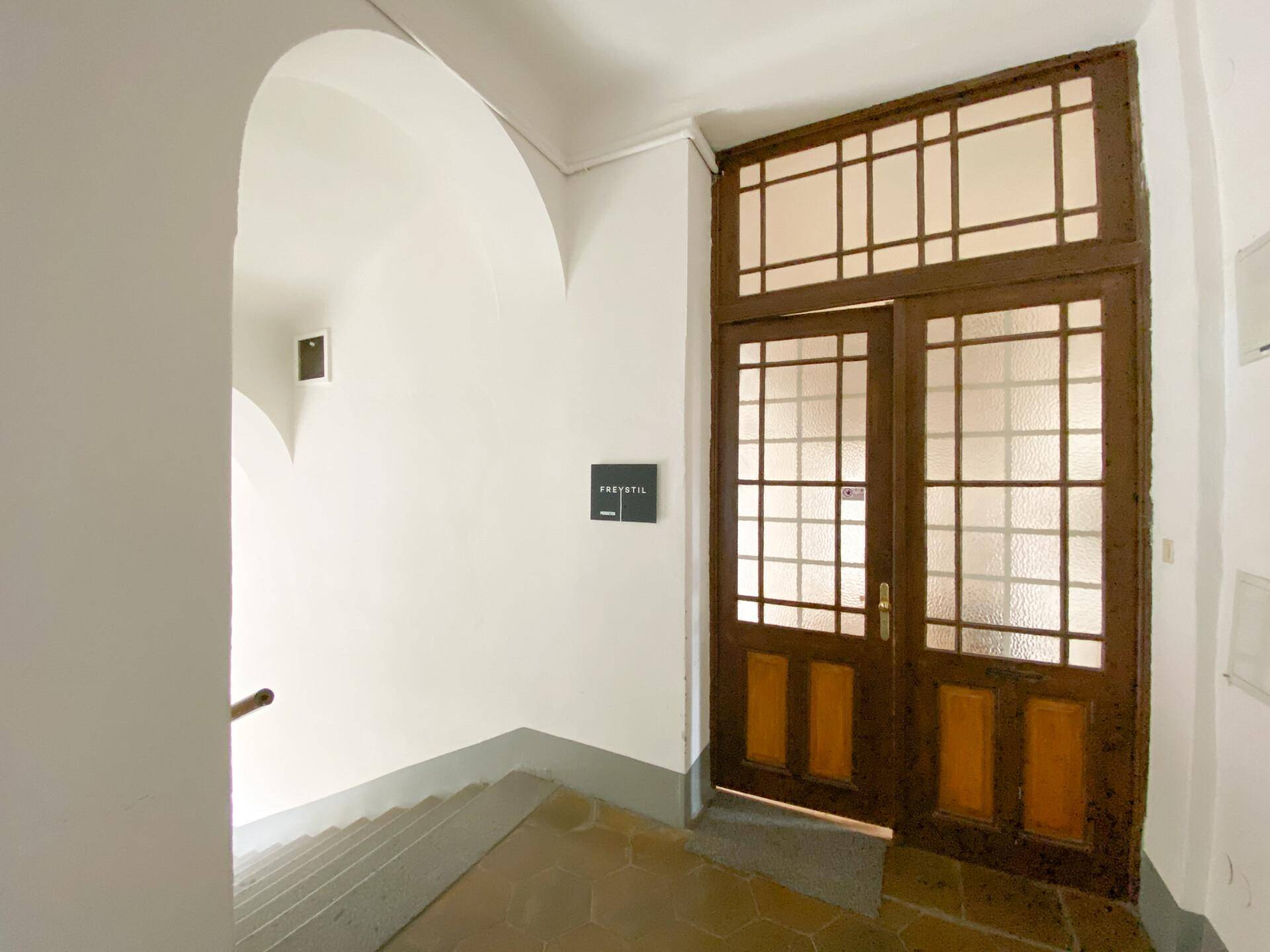 Historisches Treppenhaus mit gewölbter Decke und einer verzierten Doppeltür aus Holz mit Glaseinsätzen.