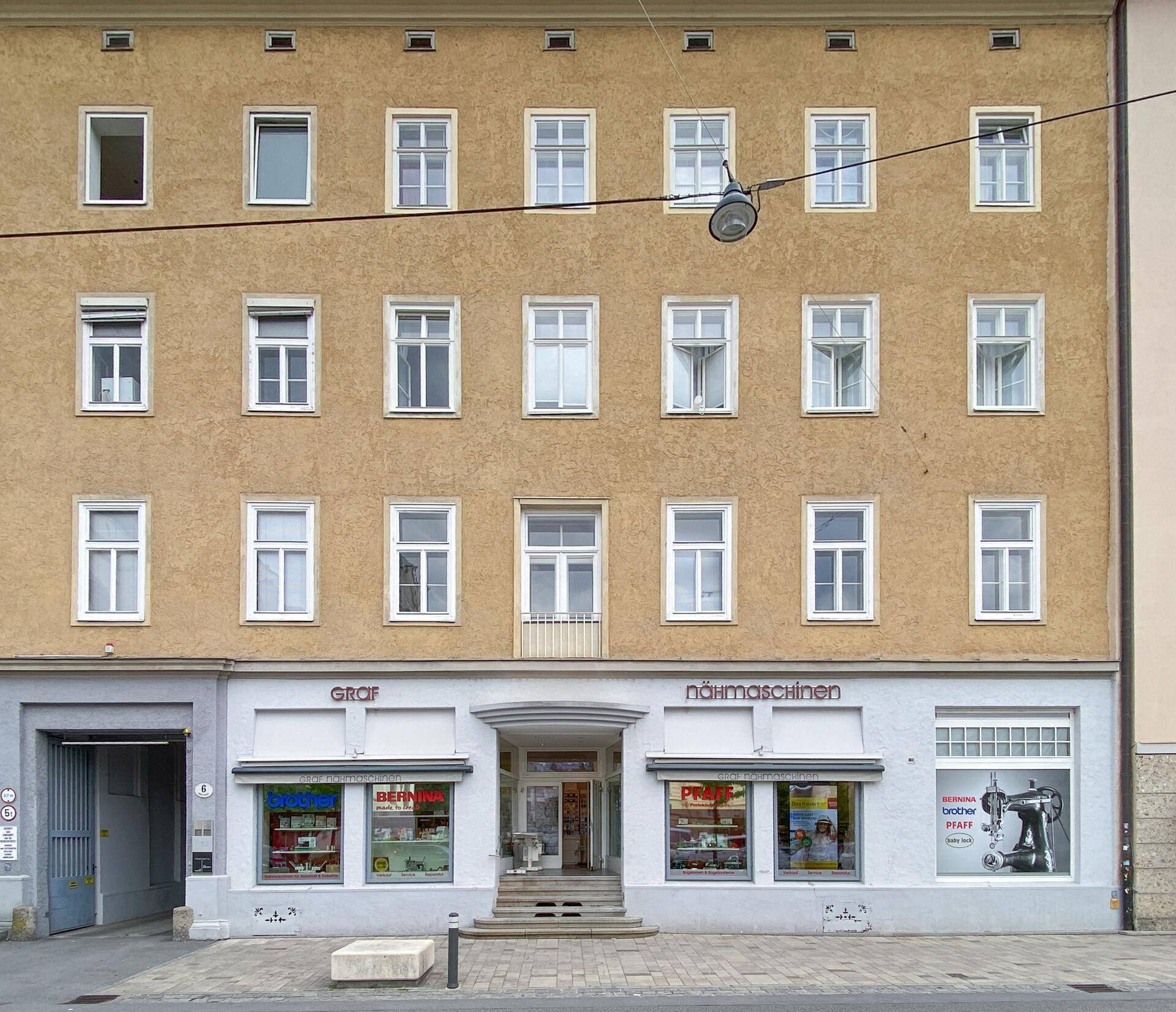 Fassade eines mehrstöckigen Gebäudes mit Geschäften im Erdgeschoss und zahlreichen Fenstern.
