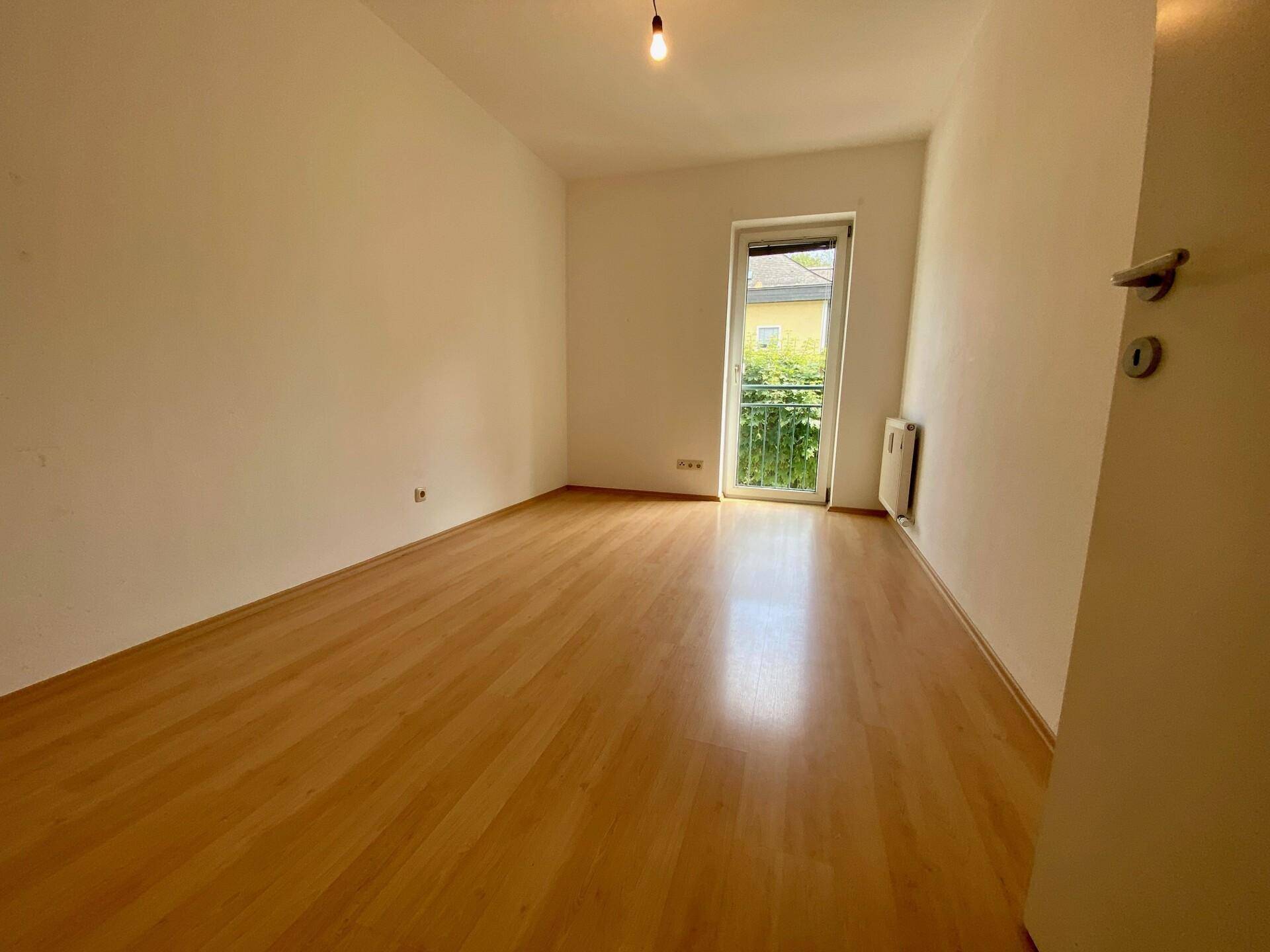 Helles Schlafzimmer mit Holzfußboden und einem Fenster, das viel natürliches Licht spendet.