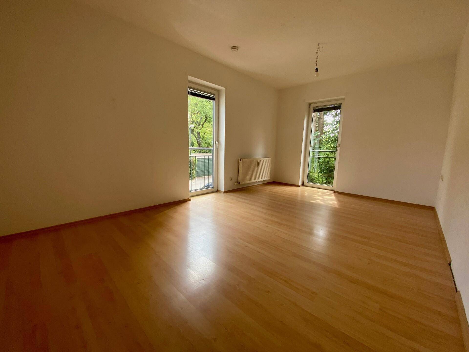 Geräumiger, heller Raum mit Holzfußboden und zwei Fenstertüren, die Zugang ins Freie bieten.