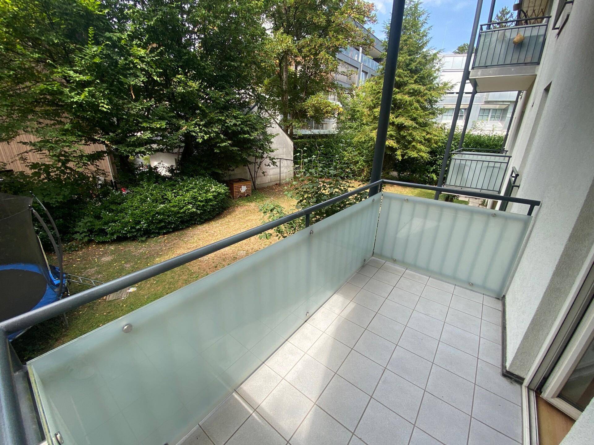 Balkon mit Fliesenboden und Milchglasbrüstung, bietet einen Blick auf den grünen Gartenbereich.