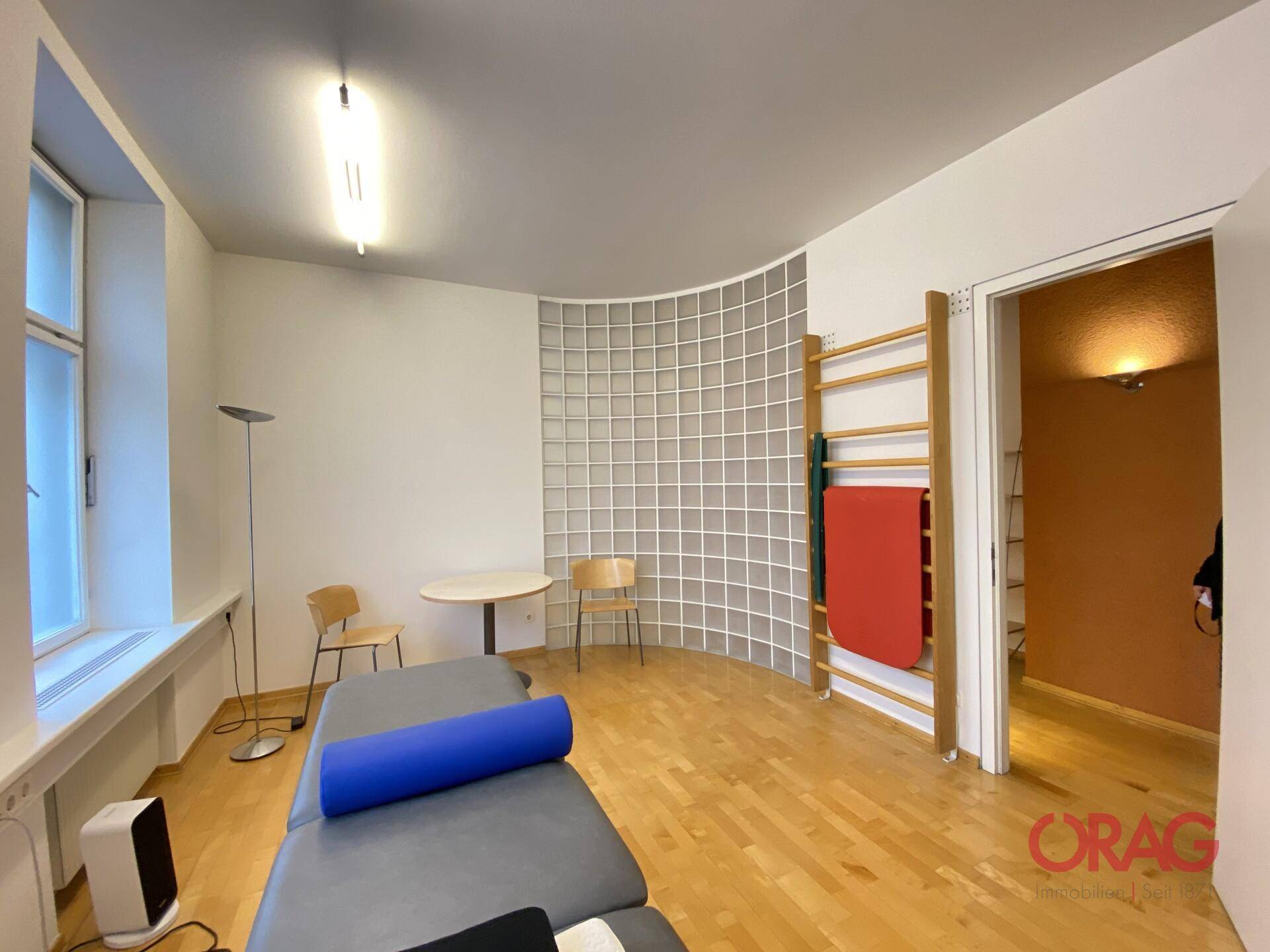 Therapieraum mit Holzboden, Sprossenwand und einer geschwungenen Glasbausteinwand für natürliches Licht.