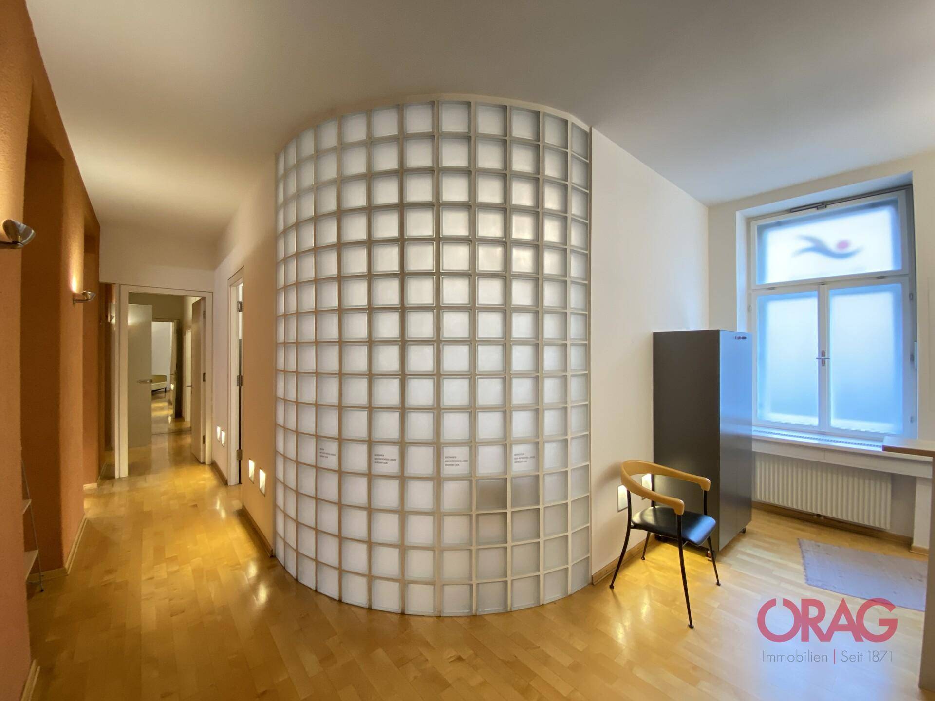 Heller Flur mit markanter geschwungener Glasbausteinwand und Holzboden in einem Bürogebäude.