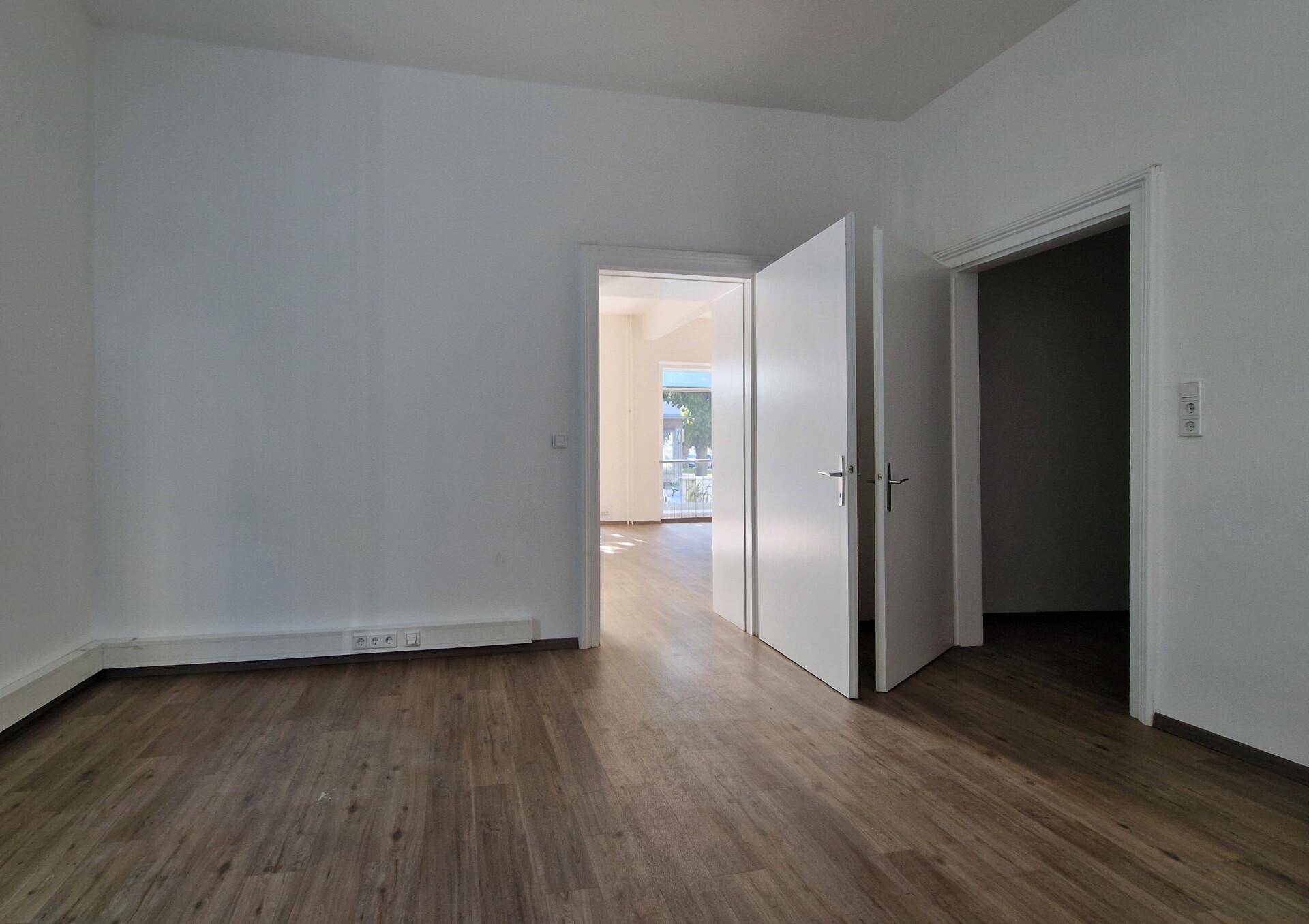 Leerer Raum mit Holzboden und zwei offenen Türen, die zu weiteren Zimmern führen.