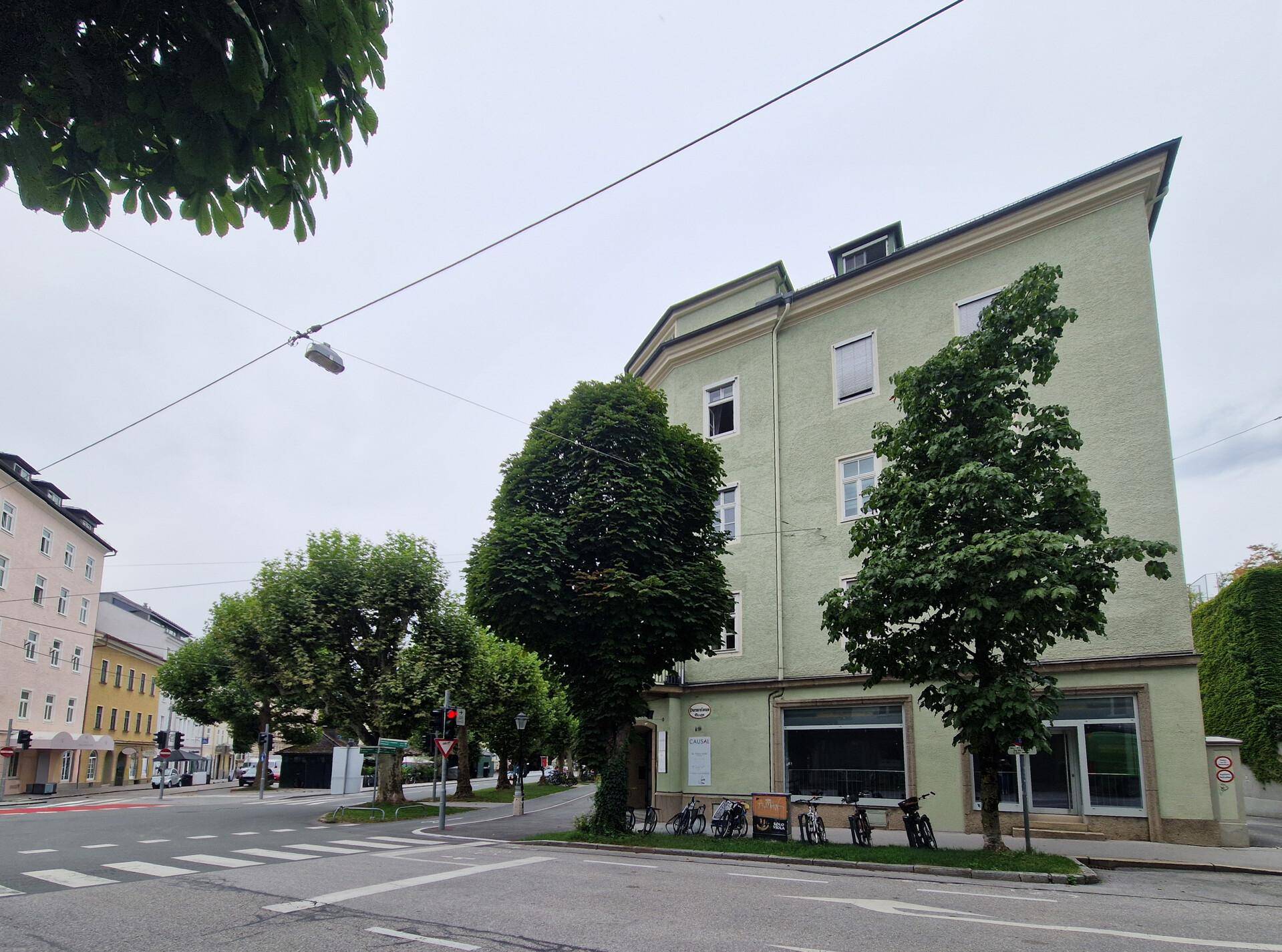Gebäude an einer Straßenecke mit hellgrüner Fassade, umgeben von Bäumen und Fahrrädern.