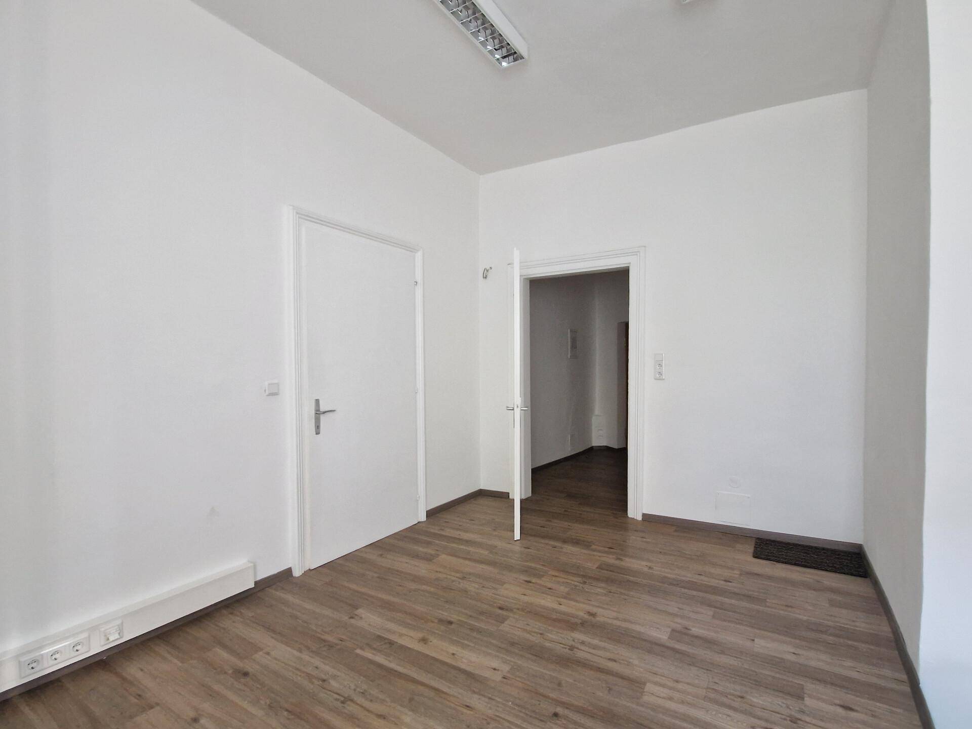 Heller Raum mit Holzboden, weißen Wänden und zwei Türen, ausgestattet mit Deckenbeleuchtung.