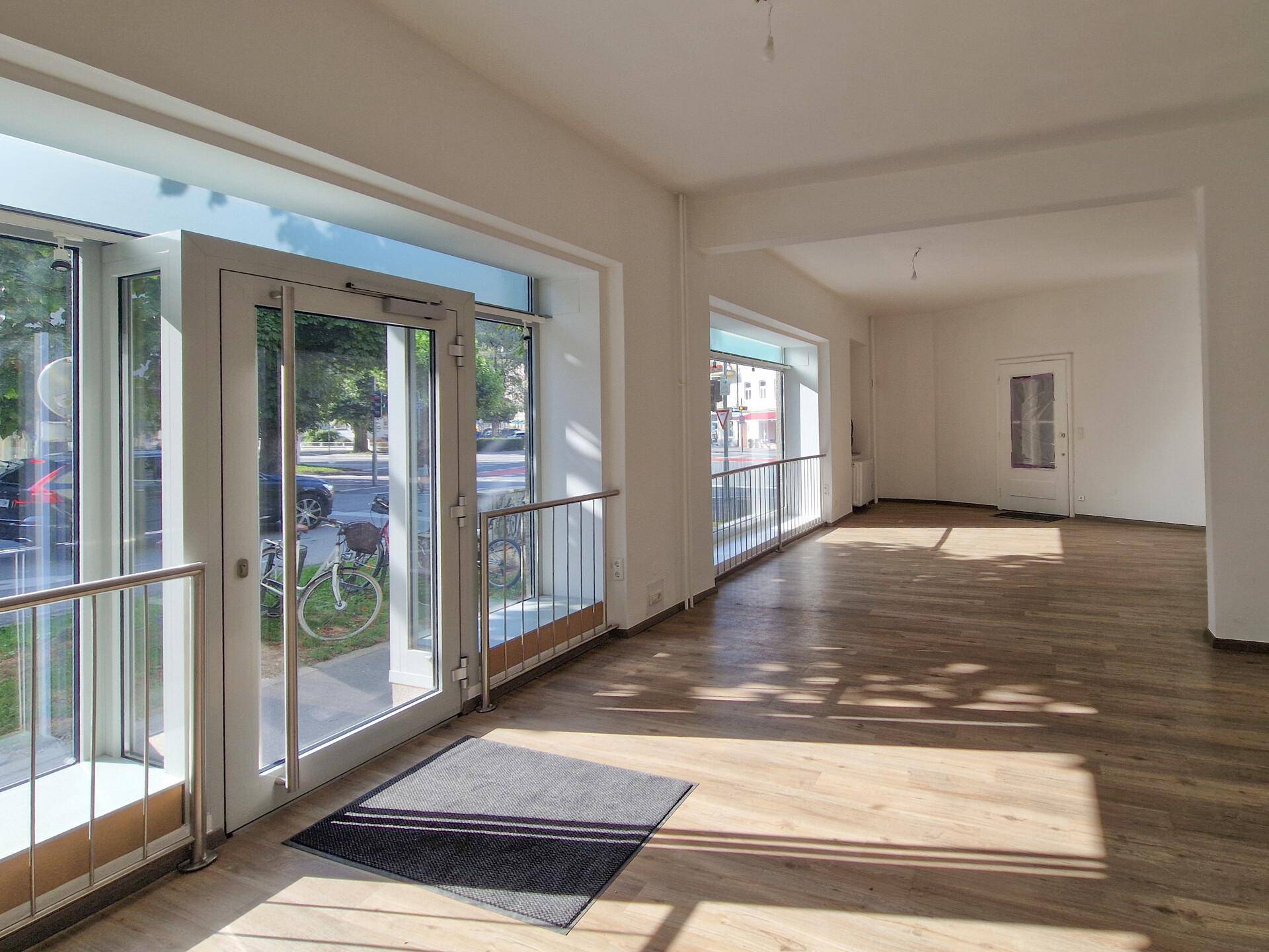 Heller und offener Geschäftsraum mit großen Schaufenstern zur Straße und modernem Holzboden.
