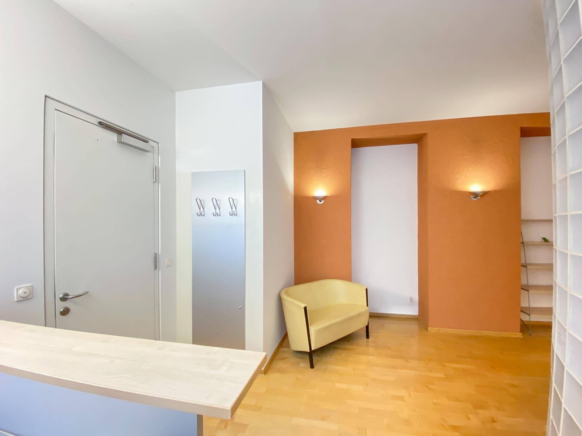 Eingangsbereich mit Garderobe, orangefarbener Akzentwand und Holzboden.