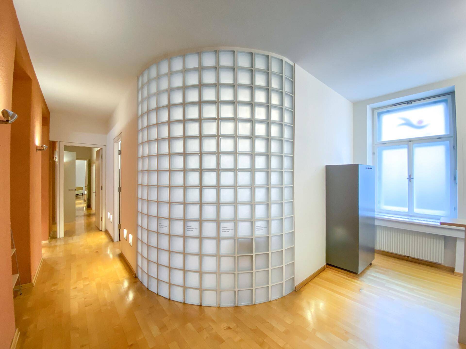 Heller Empfangsbereich mit geschwungener Glasbausteinwand und Holzboden.