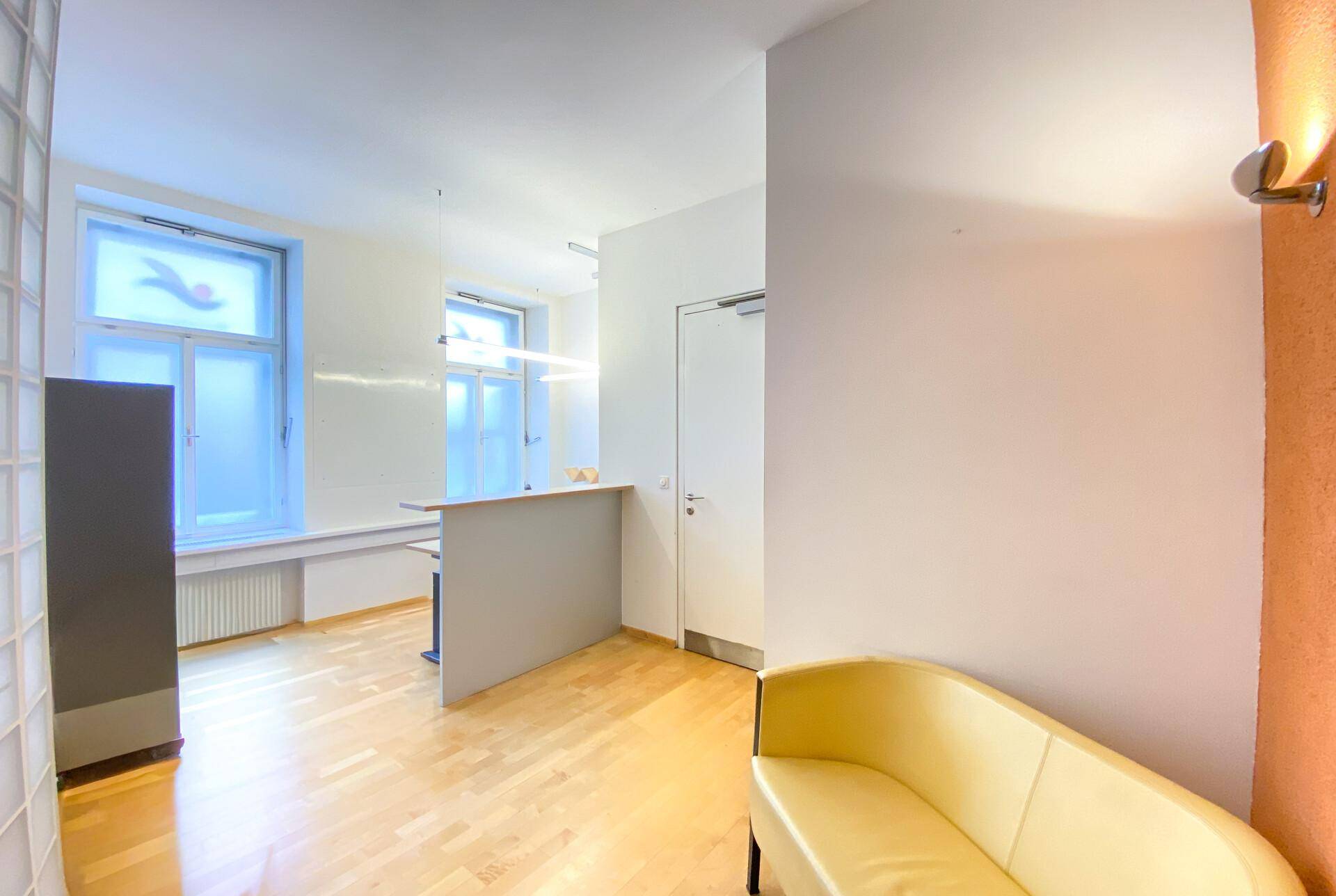 Empfangsbereich mit kleiner Theke, Sitzgelegenheit und Fenstern für natürliches Licht.