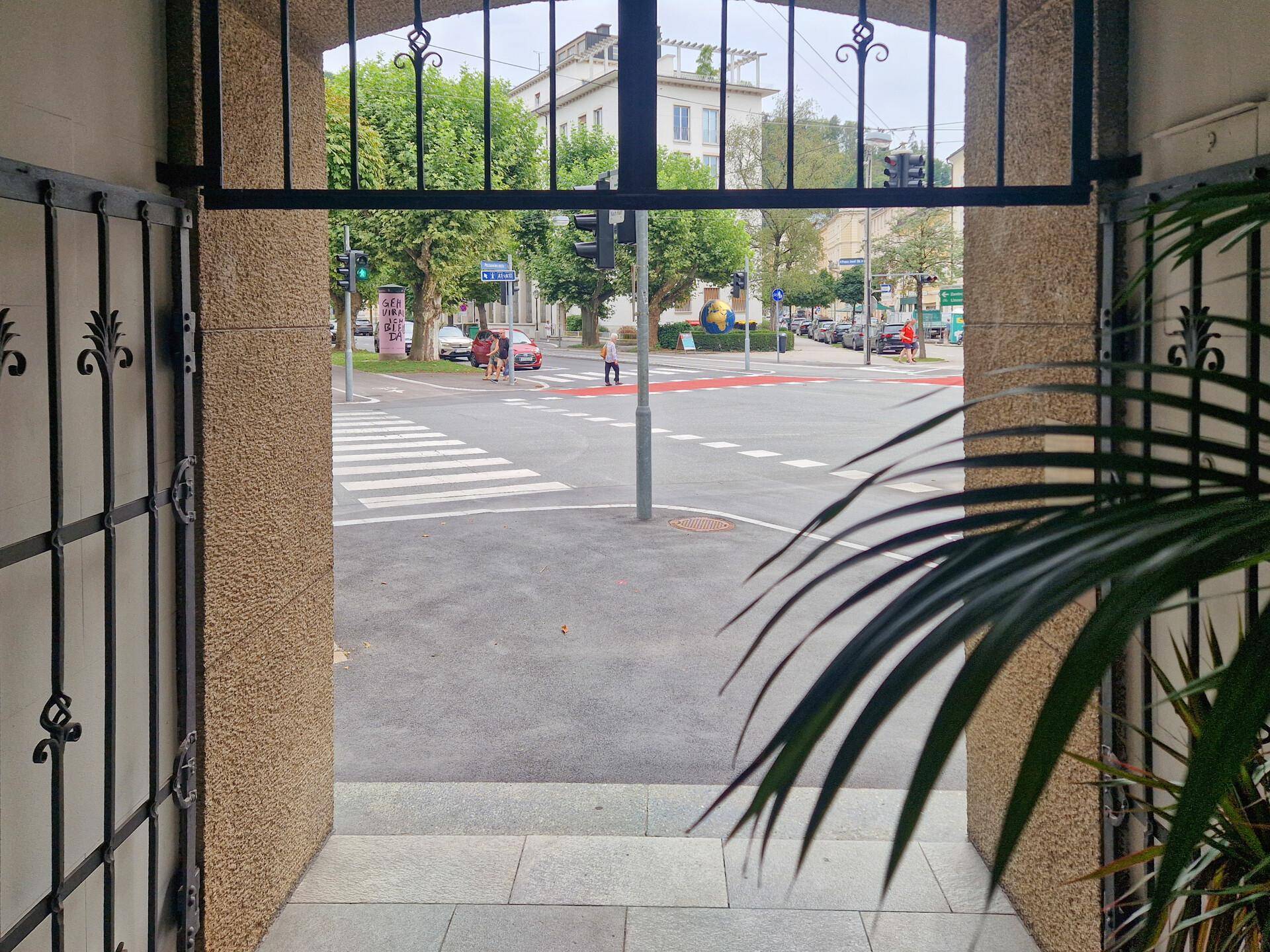 Blick vom Eingangsbereich auf eine belebte Straßenkreuzung mit Zebrastreifen und Ampeln.