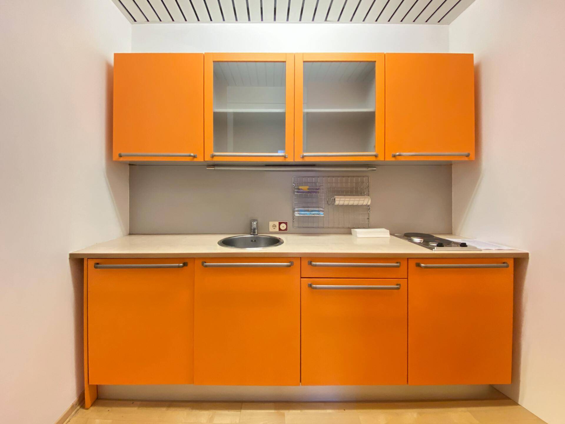 Kleine Küchenzeile mit leuchtend orangefarbenen Schränken und Spülbecken.