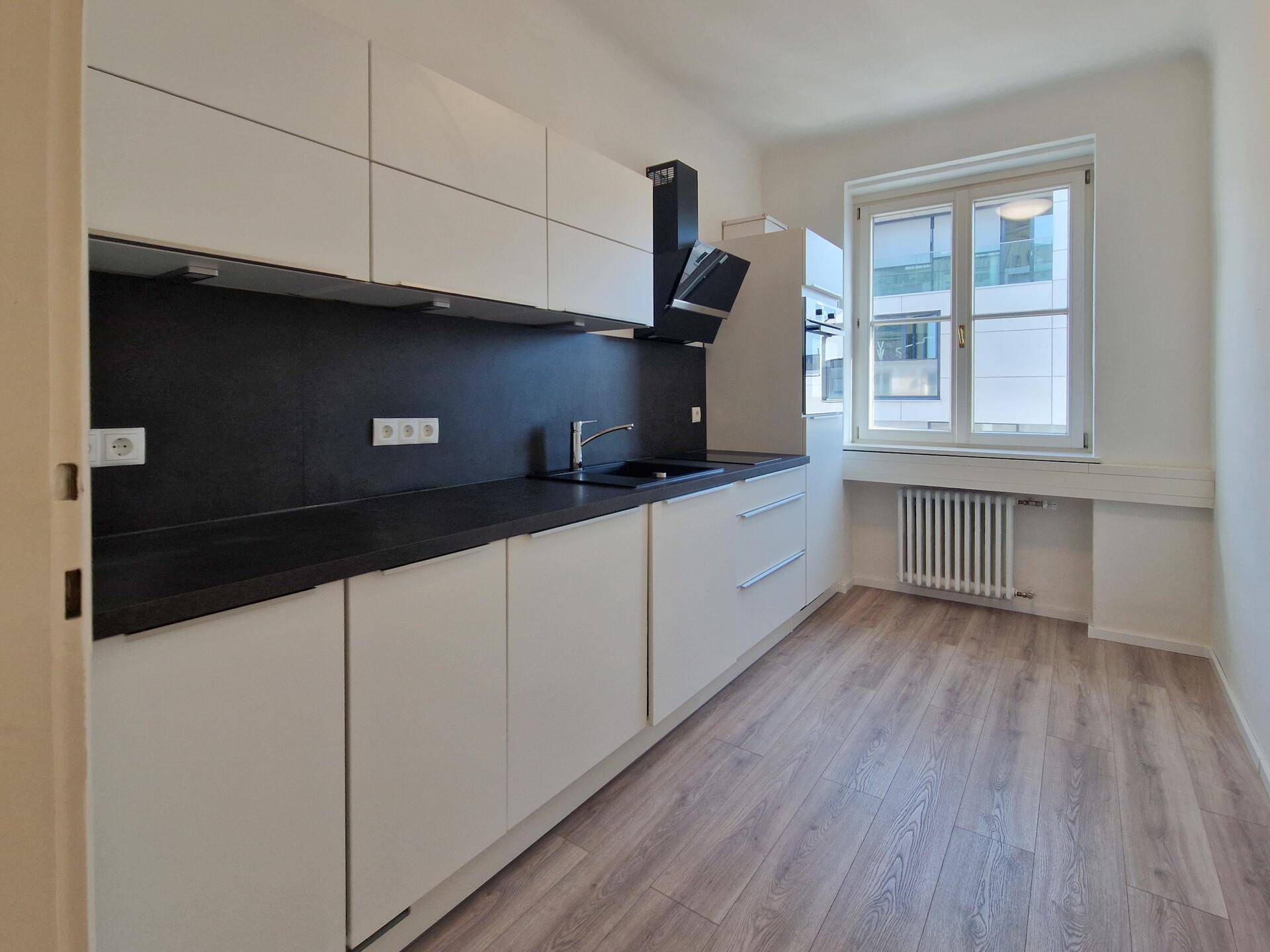 Moderne Küche mit weißen, grifflosen Schränken, schwarzer Arbeitsplatte und Laminatboden.