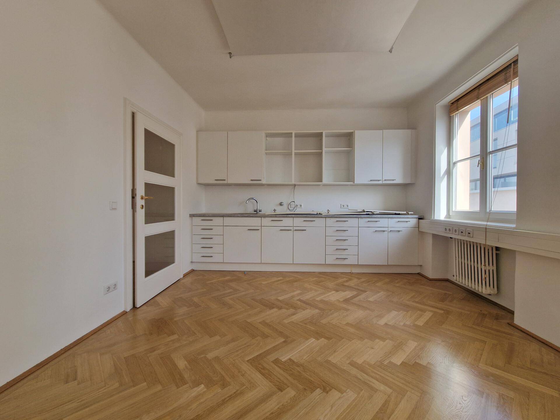 Helle Küche mit weißen Einbauschränken, Spüle und Fischgrätparkett, bereit zur Nutzung.