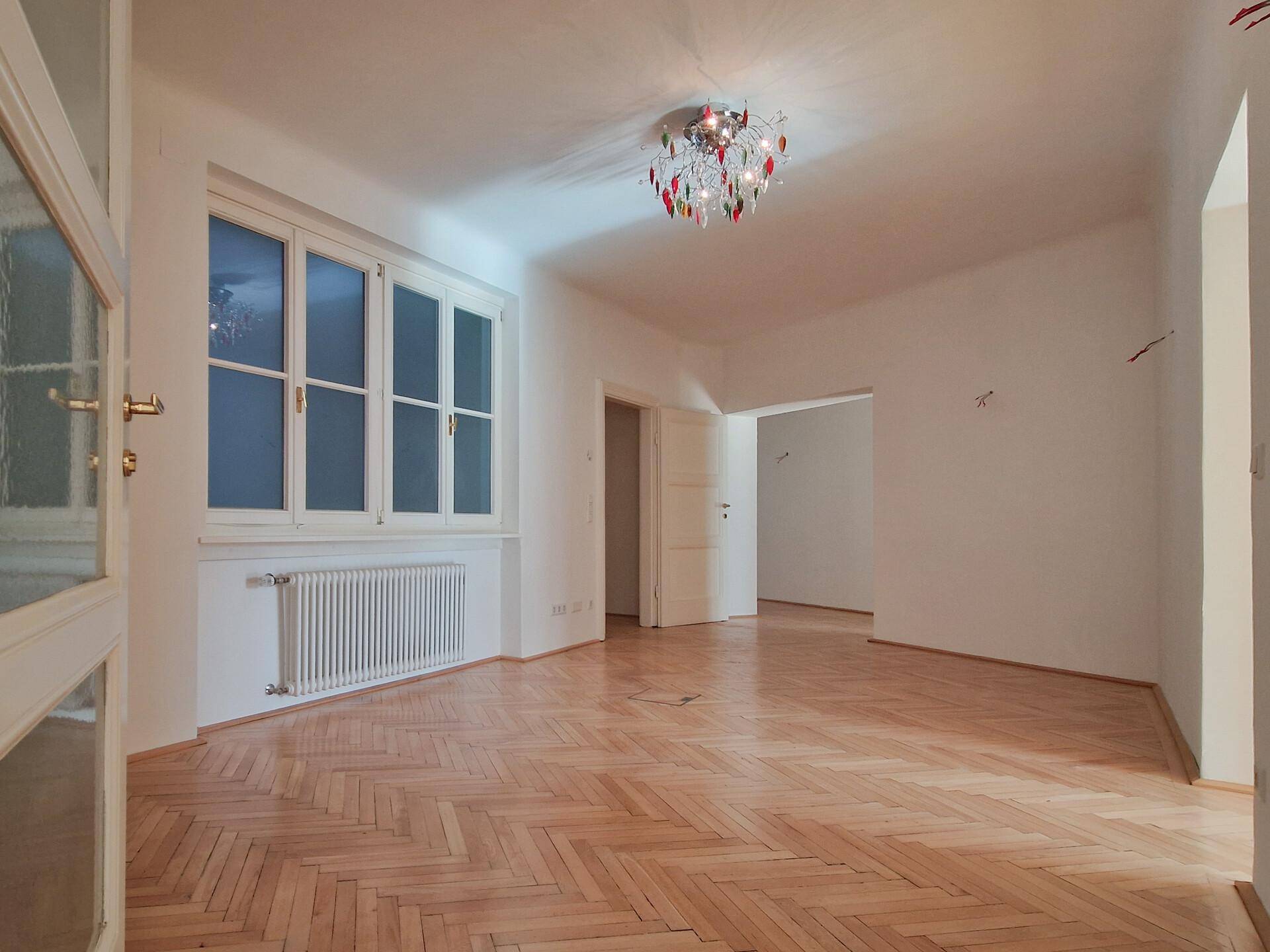 Heller Raum mit Fischgrätparkett, einem Fenster und einer dekorativen Deckenleuchte.