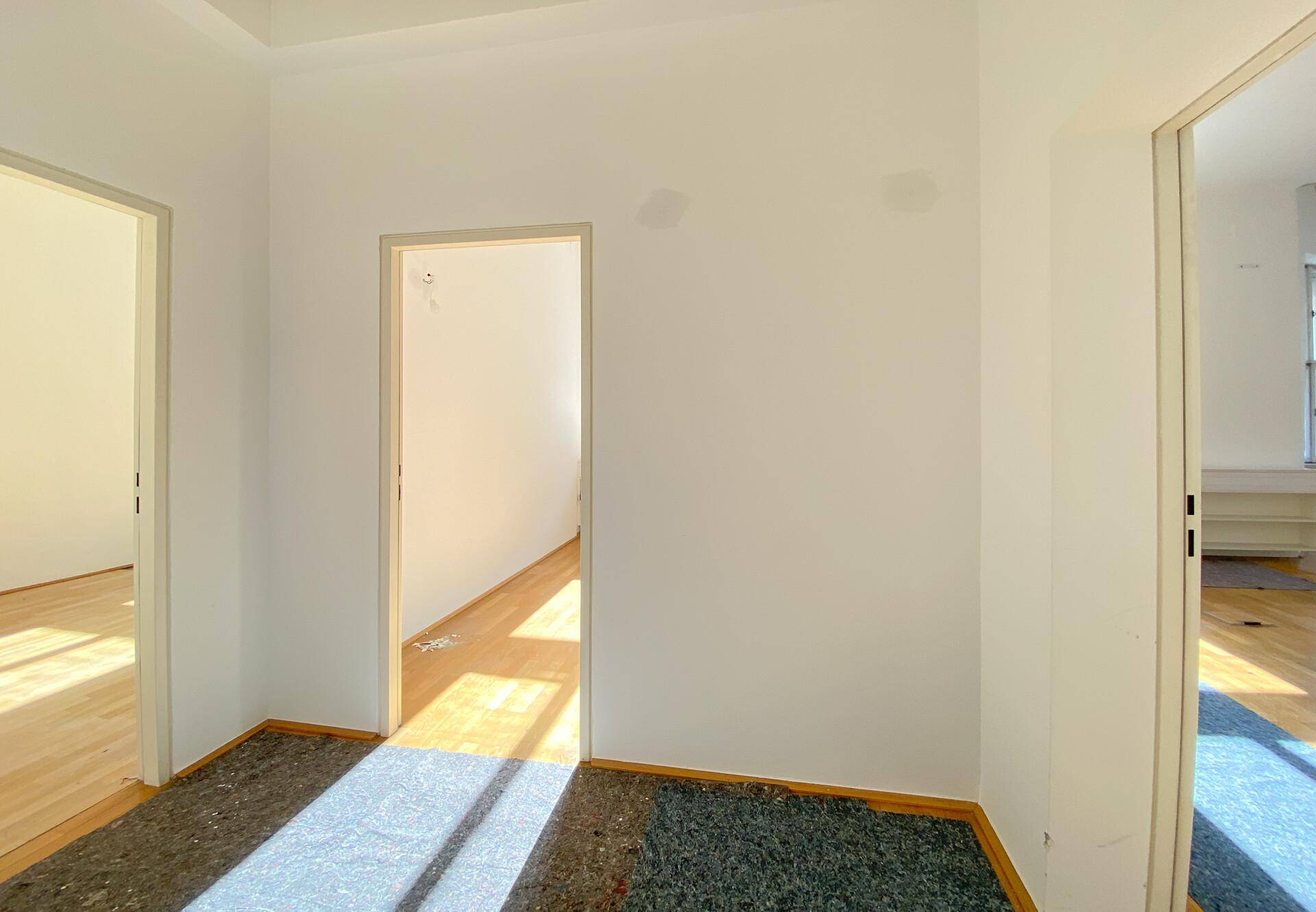 Flurbereich mit Holzboden und Teppichresten, der zu mehreren Büroräumen führt.