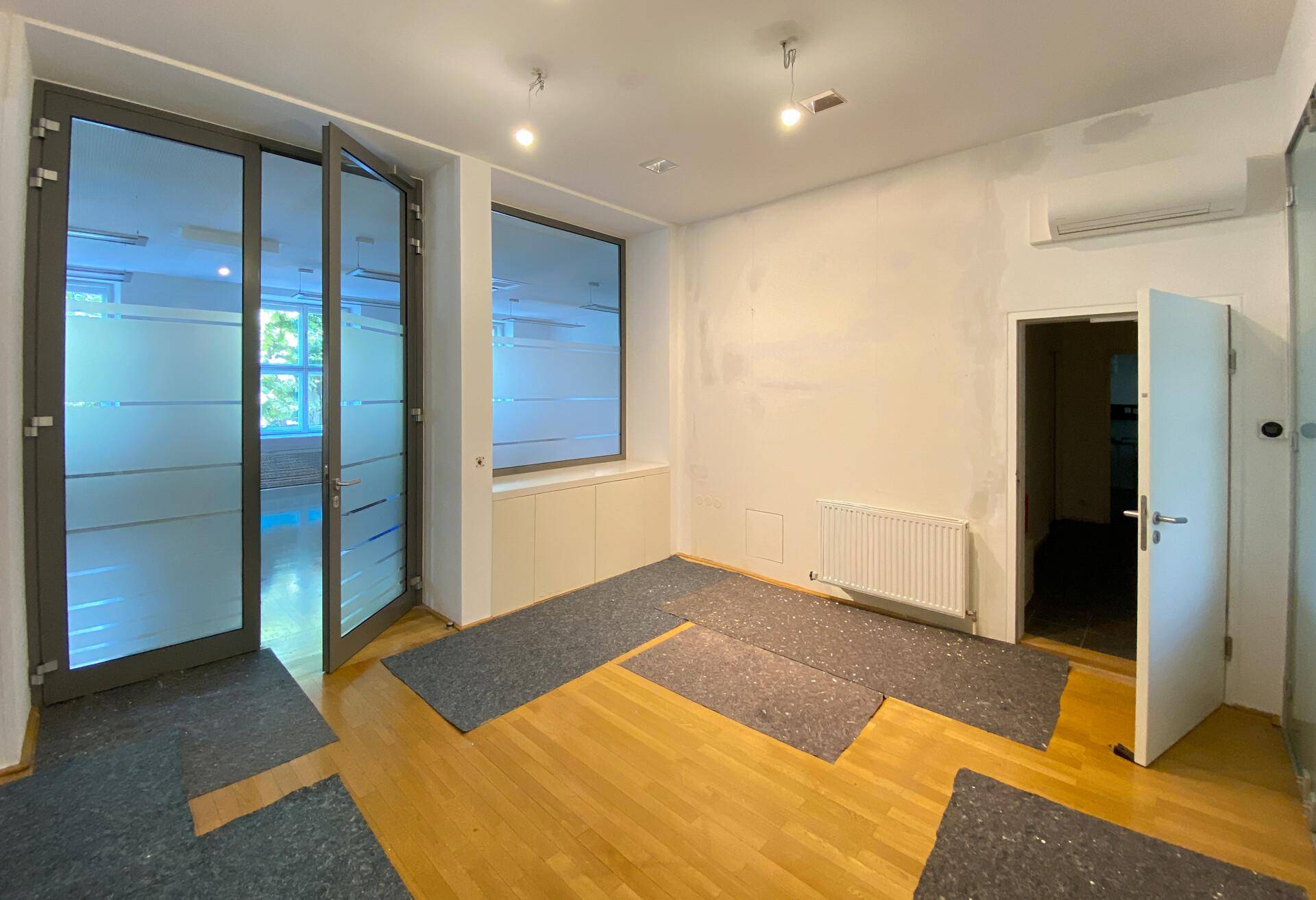 Büroraum mit Holzboden, großen Glastüren und Fenstern mit Sichtschutzfolie.