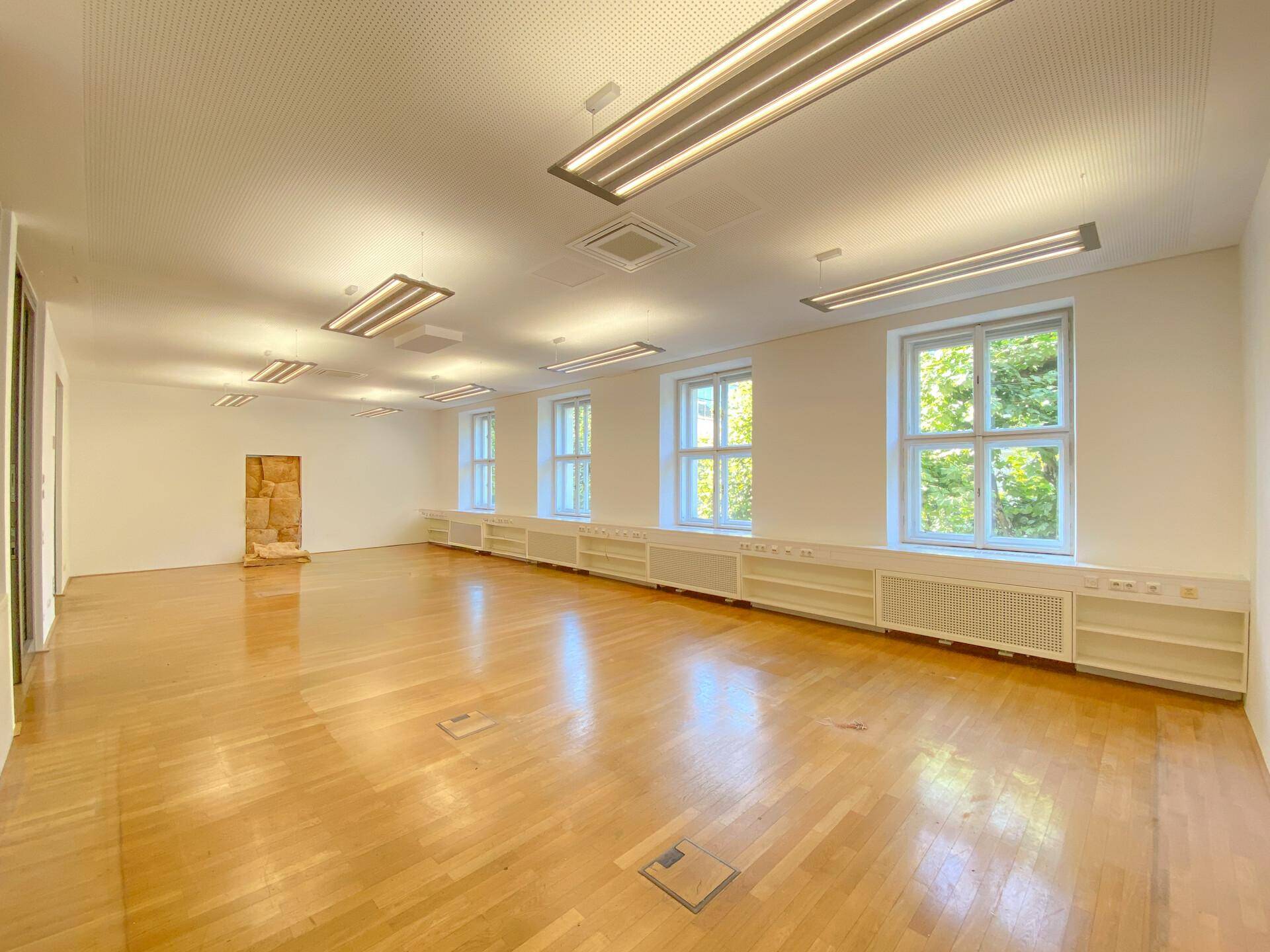 Großes, helles Büro mit Holzboden, vielen Fenstern und moderner Deckenbeleuchtung.