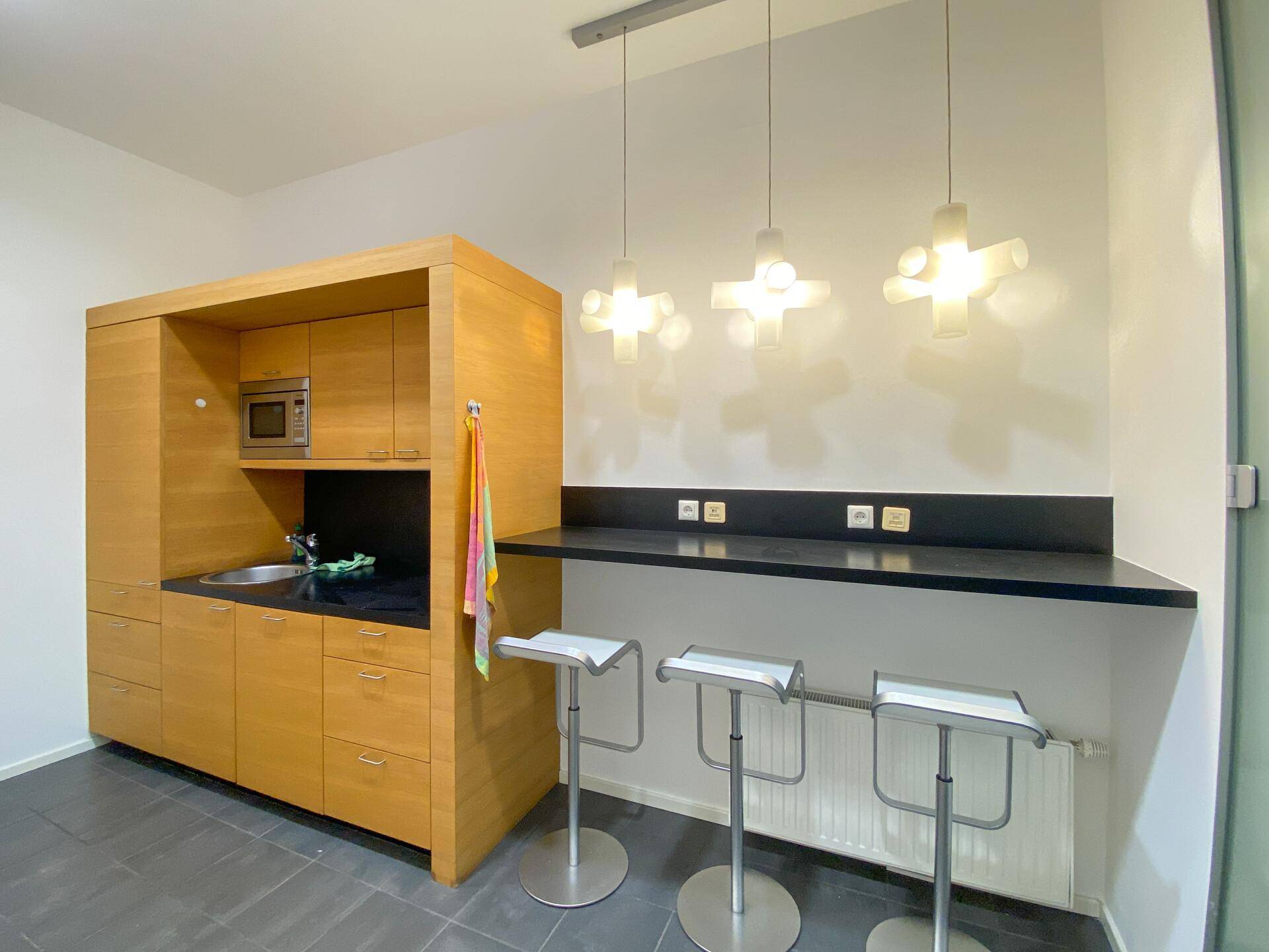 Moderne Teeküche mit Holzelementen, Mikrowelle und einer Bartheke mit Hockern.