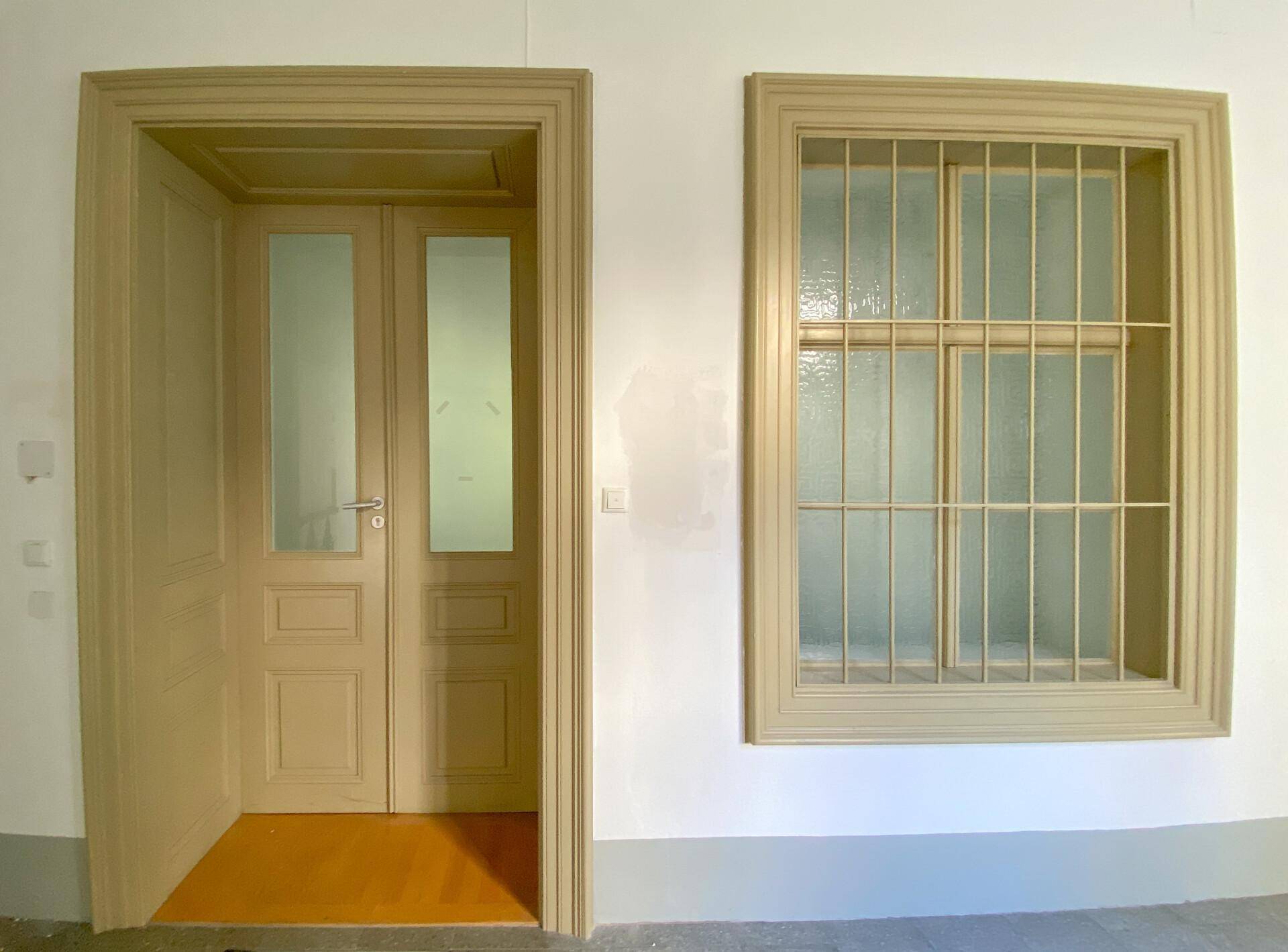 Flurbereich mit einer Doppeltür und einem Fenster mit Gitter, beide in hellem Holzrahmen.