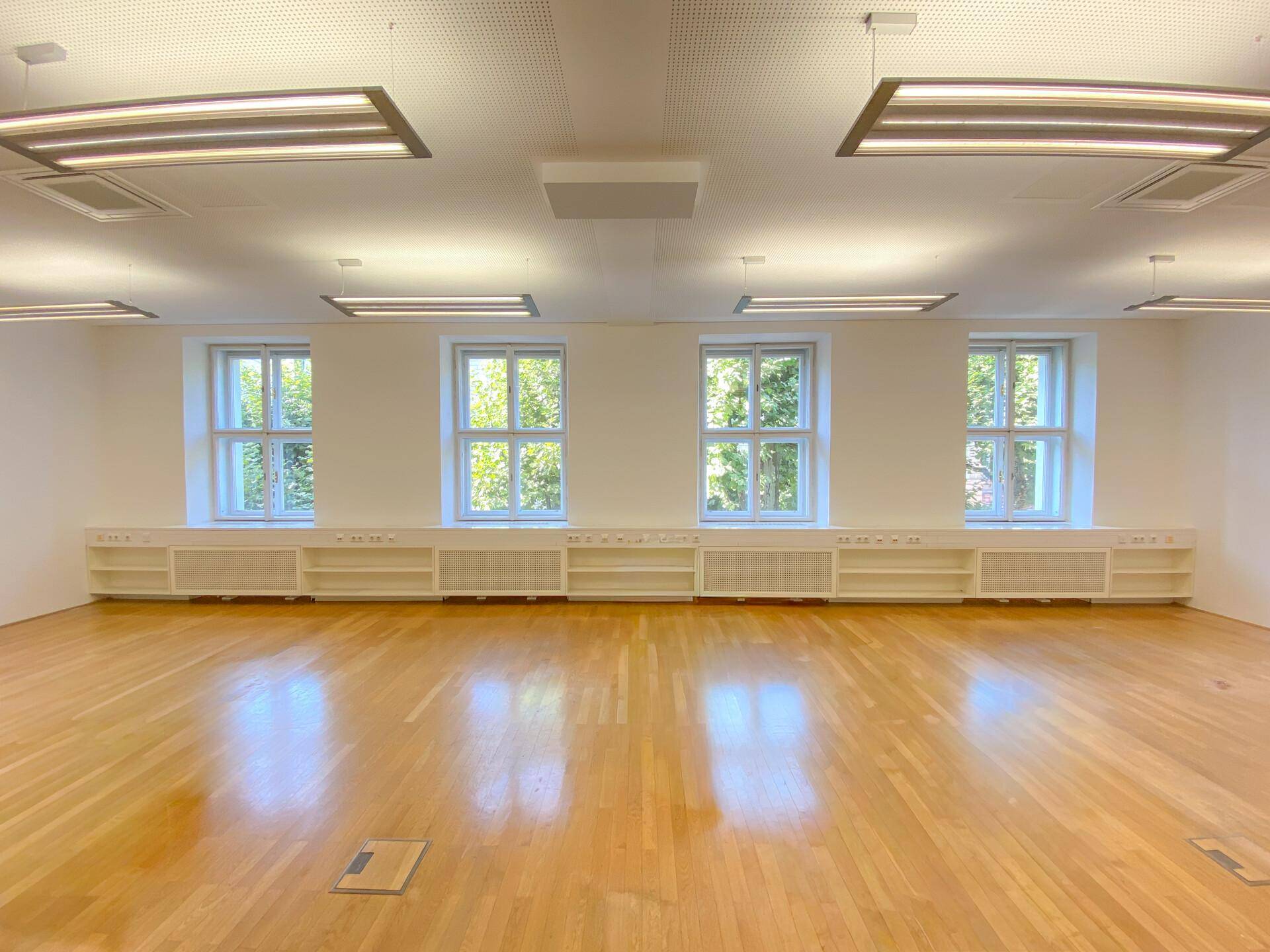 Heller Büroraum mit vier großen Fenstern, Holzboden und integrierten Heizkörperverkleidungen.