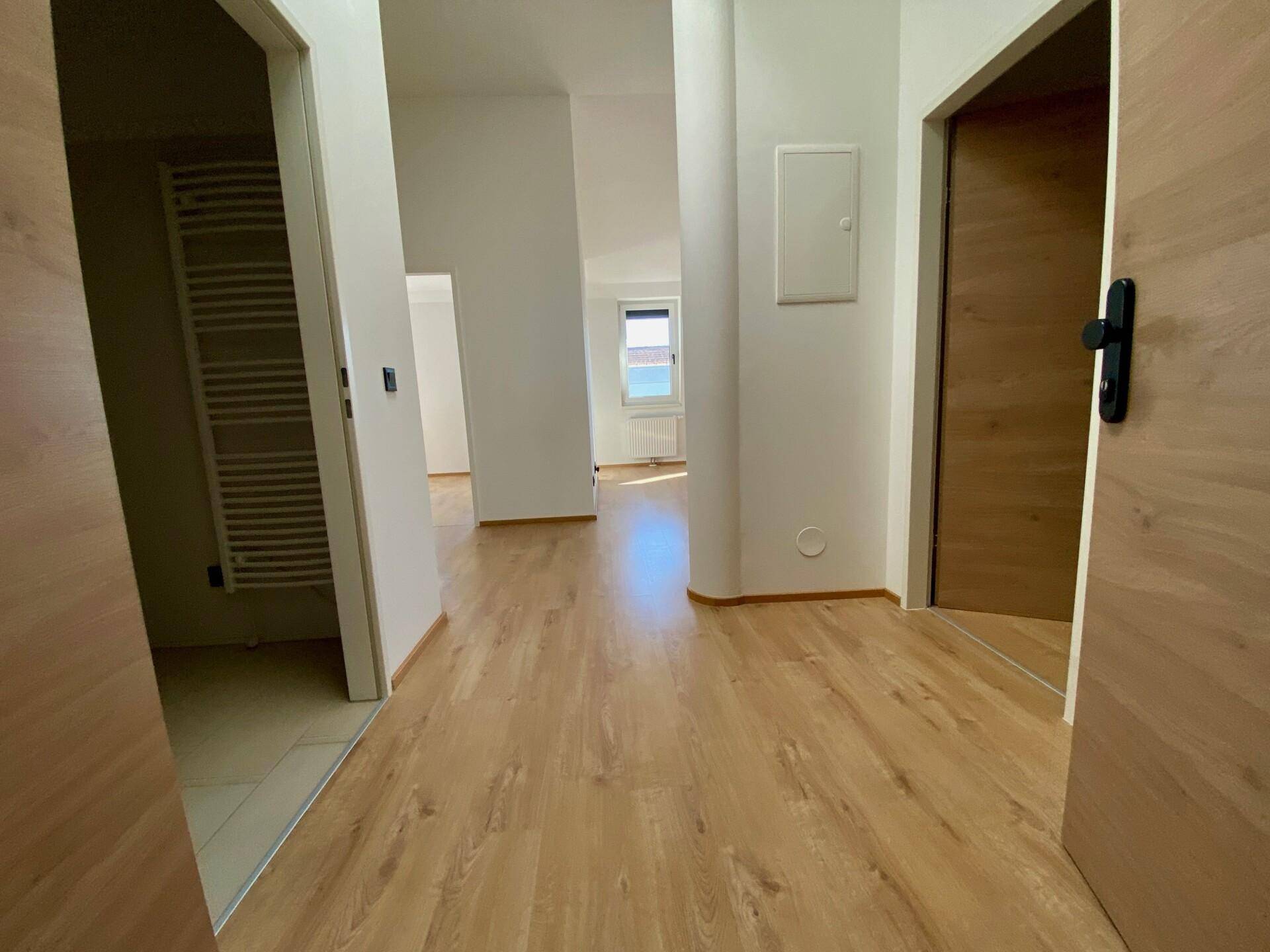 Heller Flur mit Holzfußboden, der zu verschiedenen Räumen und einem Badezimmer führt.