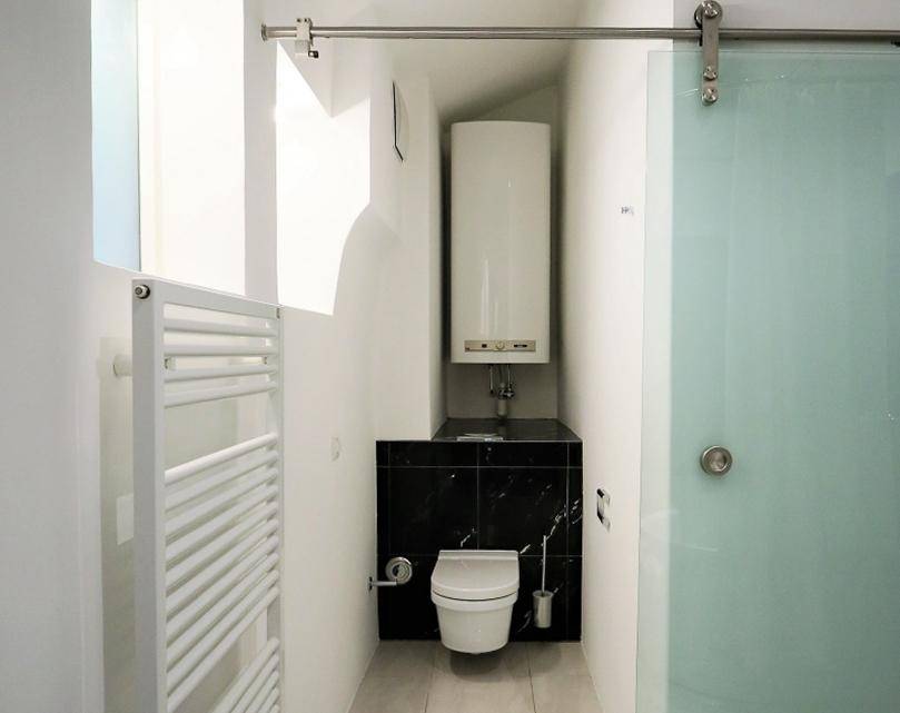 Kompaktes Gäste-WC mit Wand-WC, Handtuchheizkörper und Schiebetür.