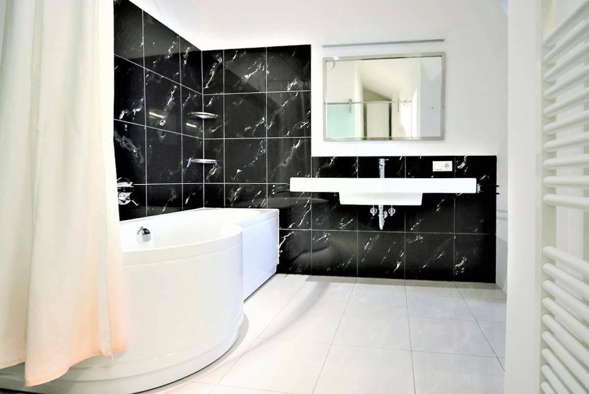 Modernes Badezimmer mit schwarzen Marmorfliesen, Badewanne und Einzelwaschbecken.