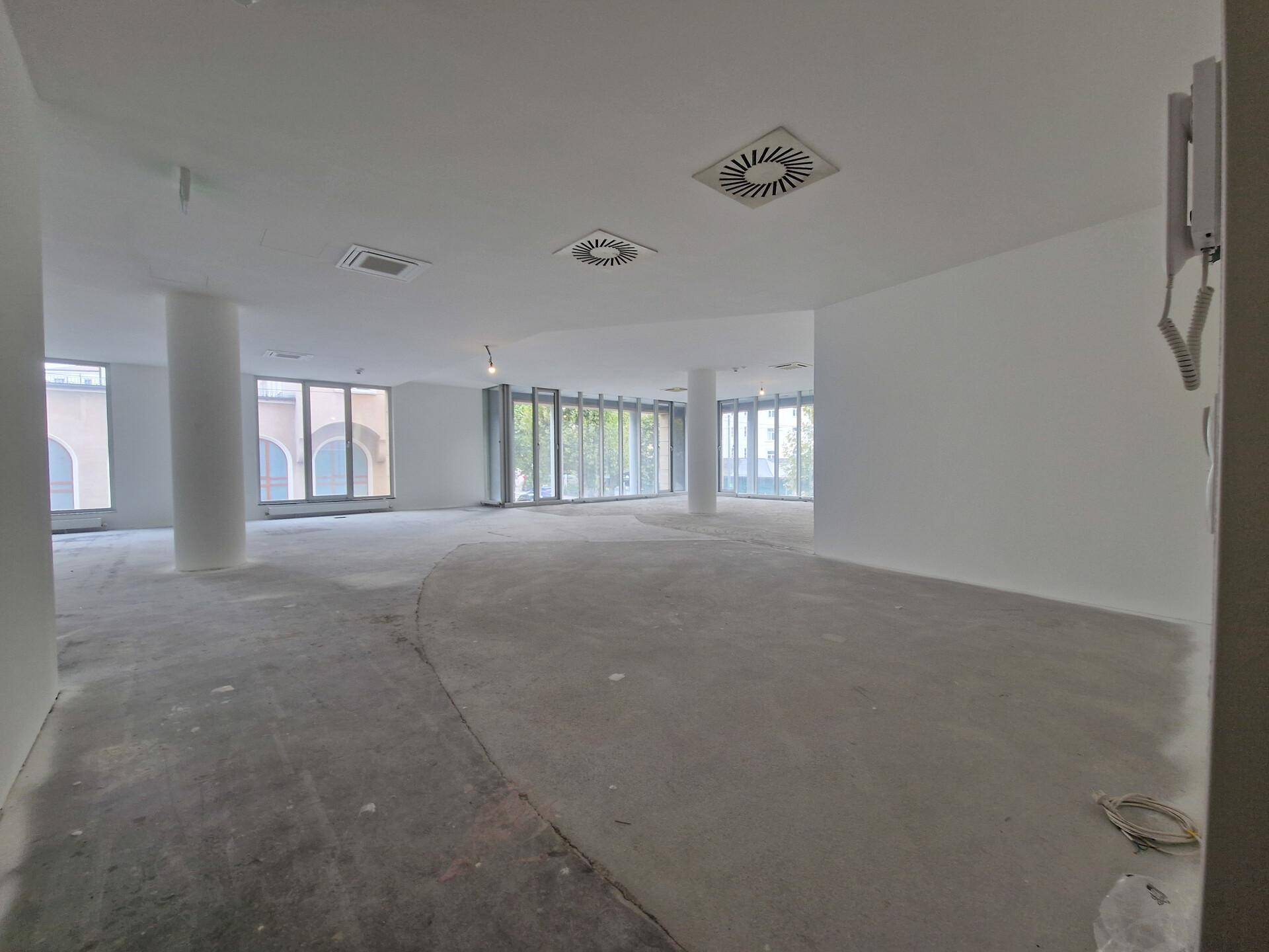 Heller, offener Büroraum mit vielen Fenstern, Säulen und sichtbaren Lüftungsauslässen an der Decke.