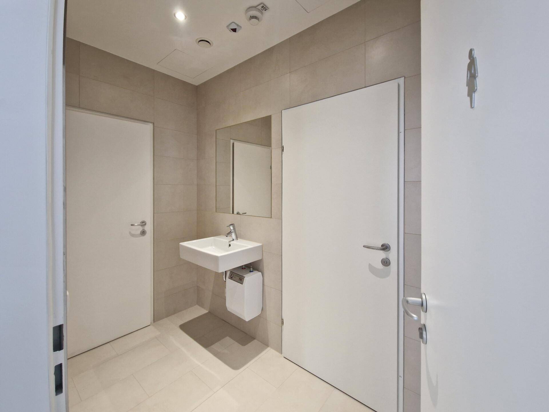 Modernes Badezimmer mit hellem Fliesenboden, Waschbecken und zwei weißen Türen.
