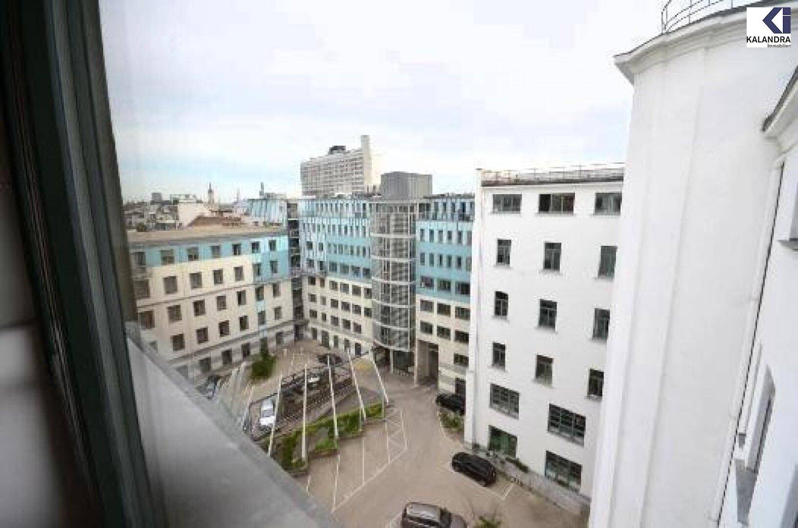 Blick aus dem Fenster auf einen Innenhof mit Parkplätzen und umliegenden modernen Bürogebäuden.